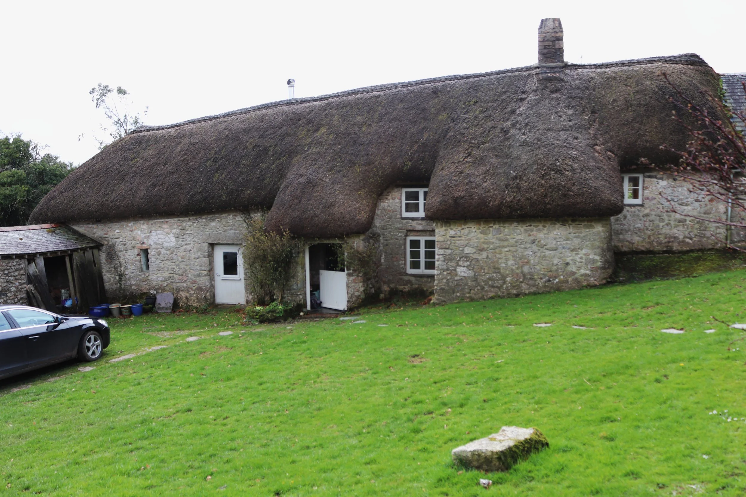 Interior of a stone church with high arched ceilings, small stained glass windows, and religious paintings. There is a wooden table with flowers and framed photos near the entrance.
