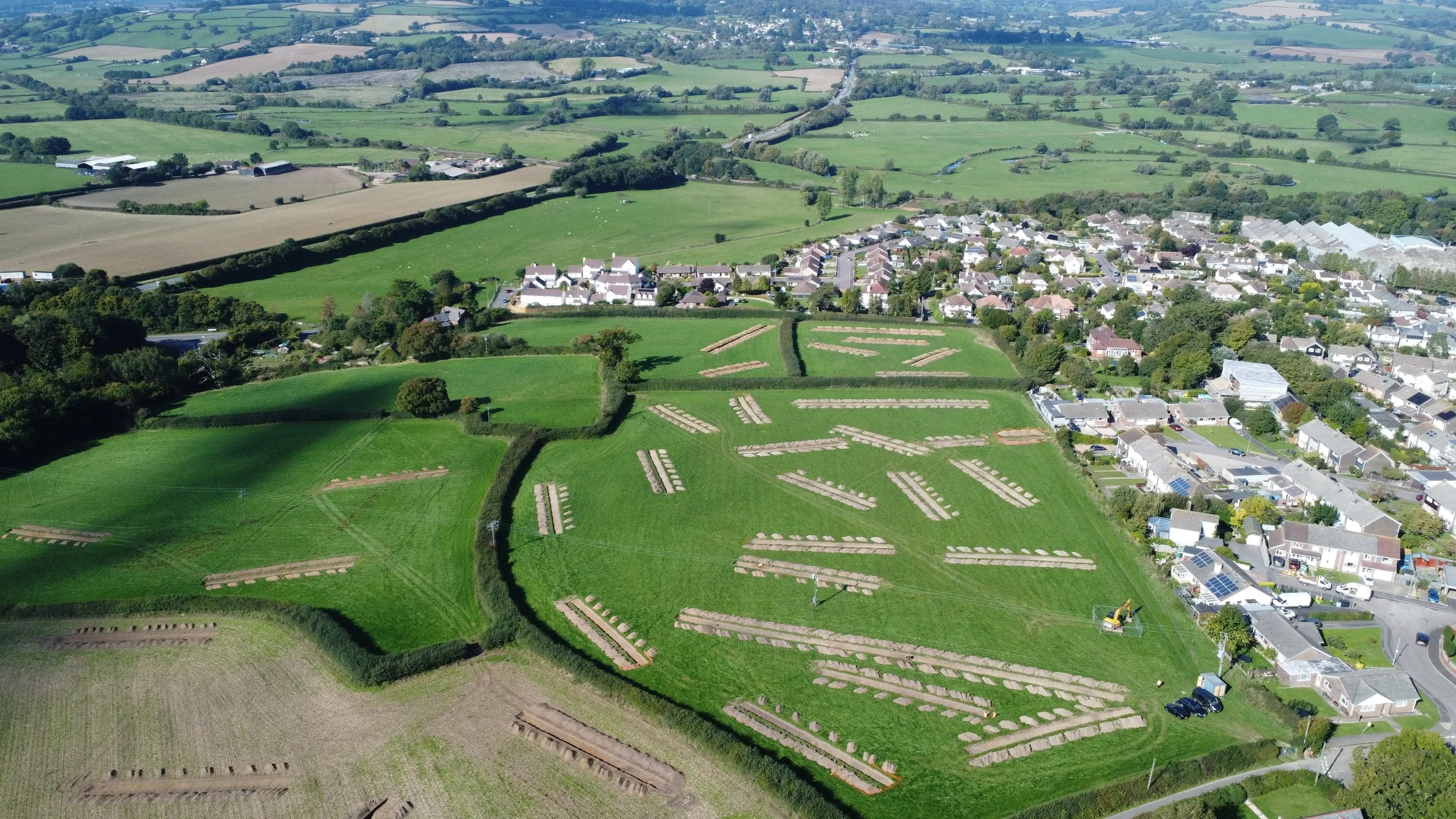Dirt trail leading into open fields and farmland, with trees on the left and grassy areas, under a partly cloudy sky.