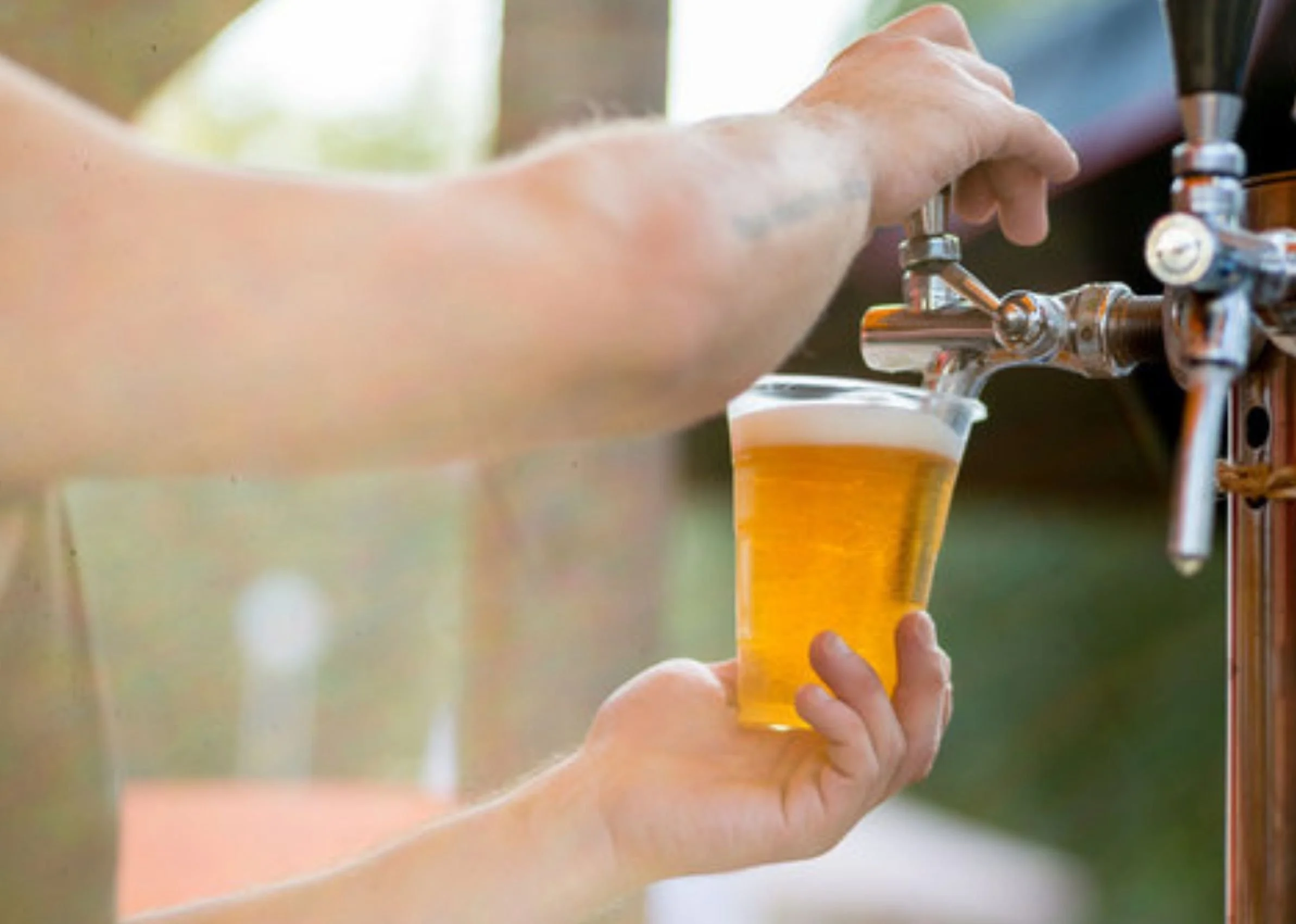 A person opening a tap to pour beer into a clear glass. The focus is on the hand and the beer glass.