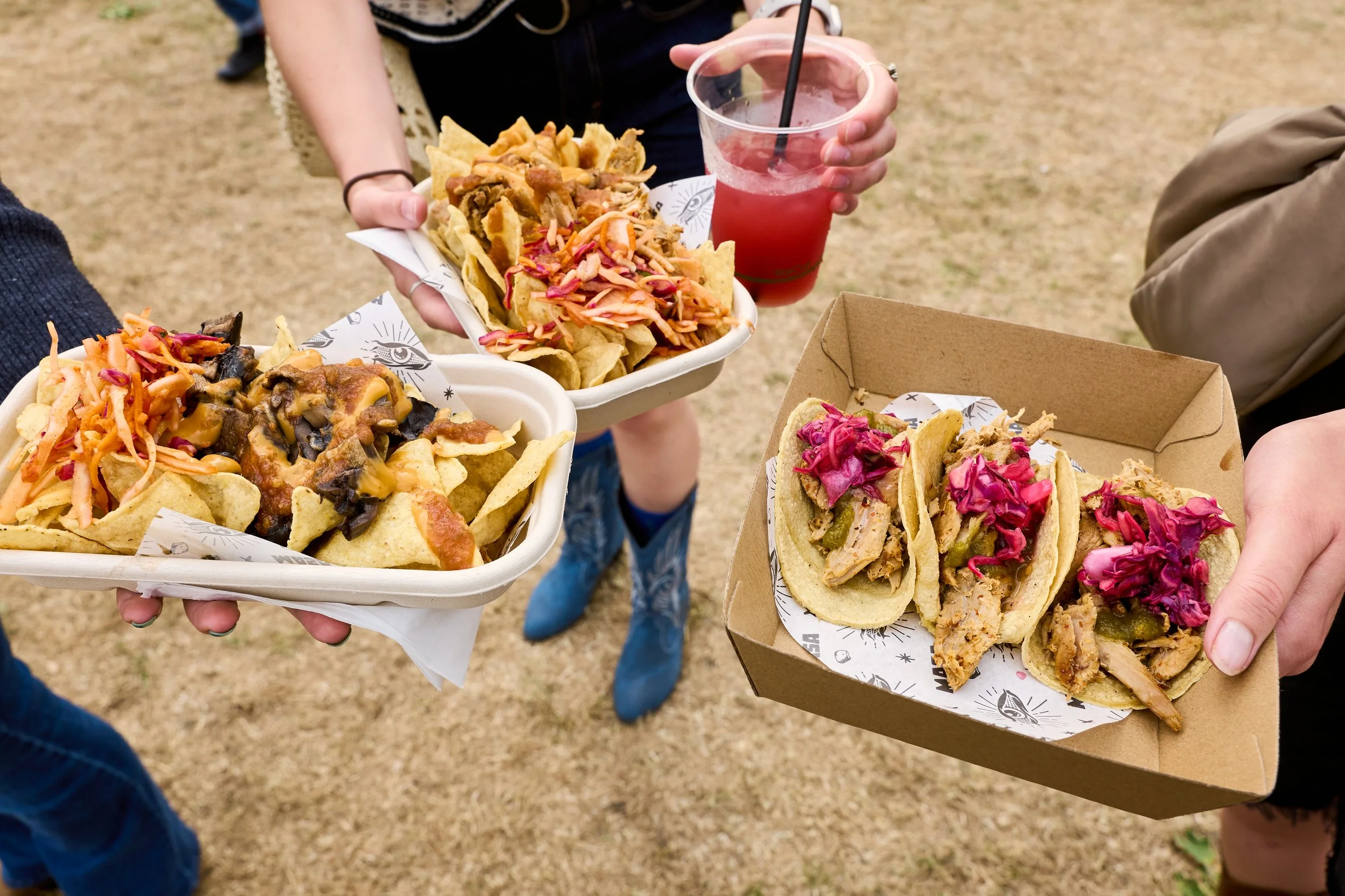 People holding food trays with tacos and nachos, and a person holding a drink at an outdoor event.