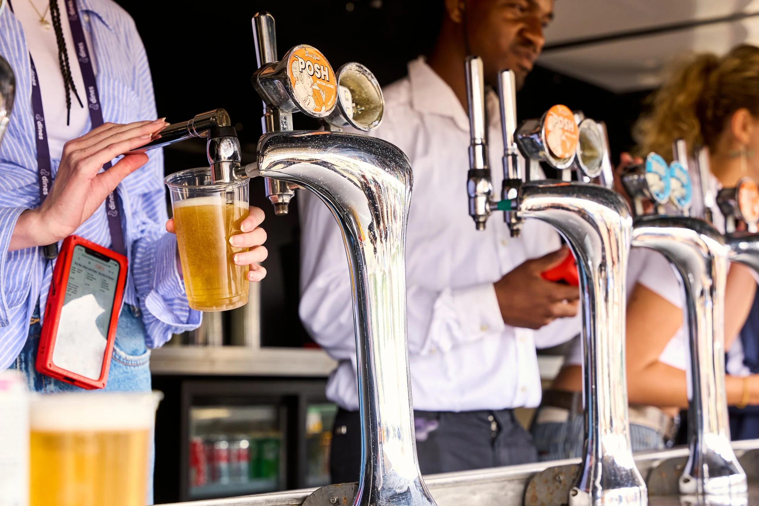 People lining up to get draft beers from taps at a bar or outdoor event.
