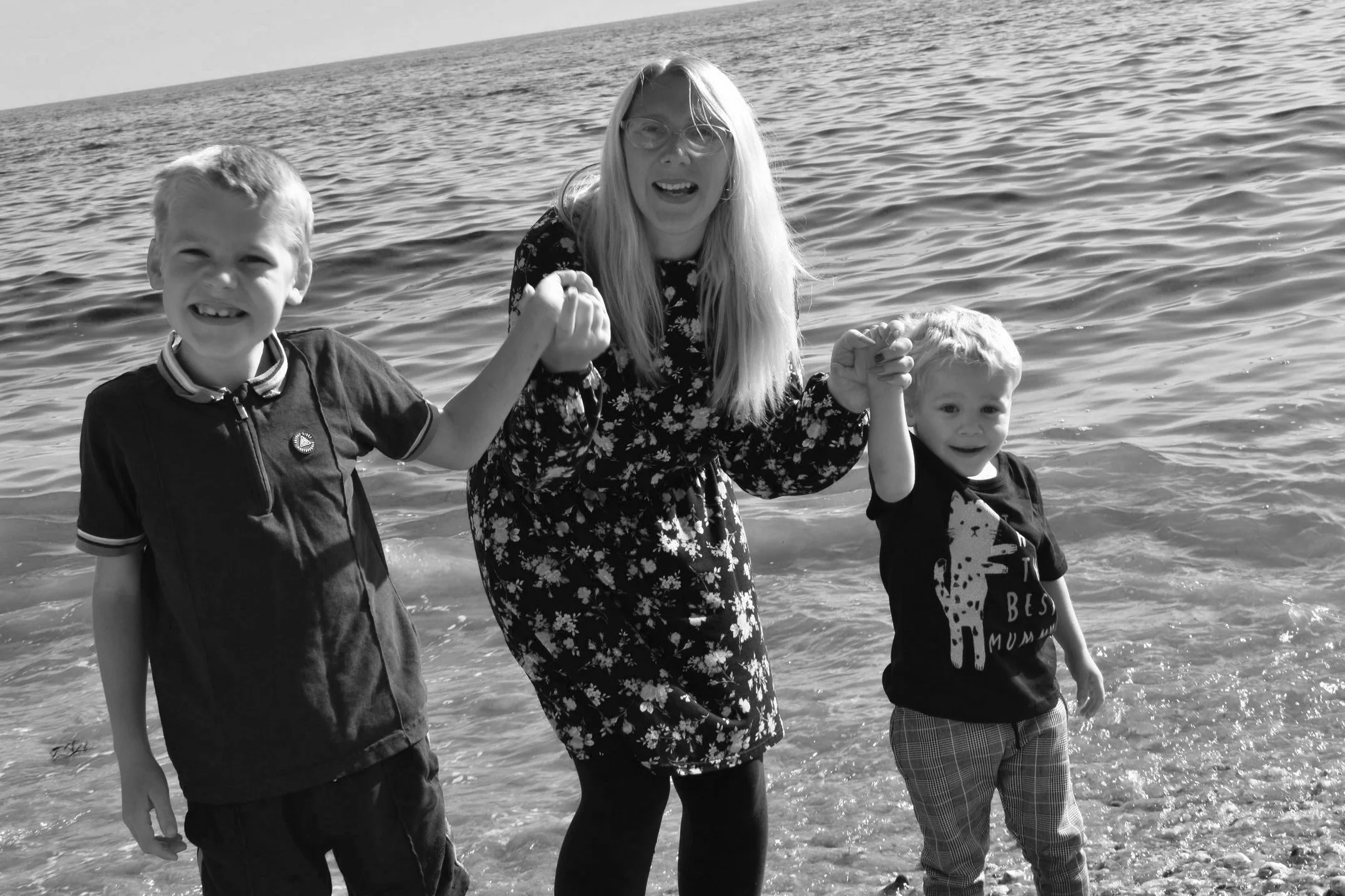 Black and white photo of a woman holding hands with two children near the ocean.