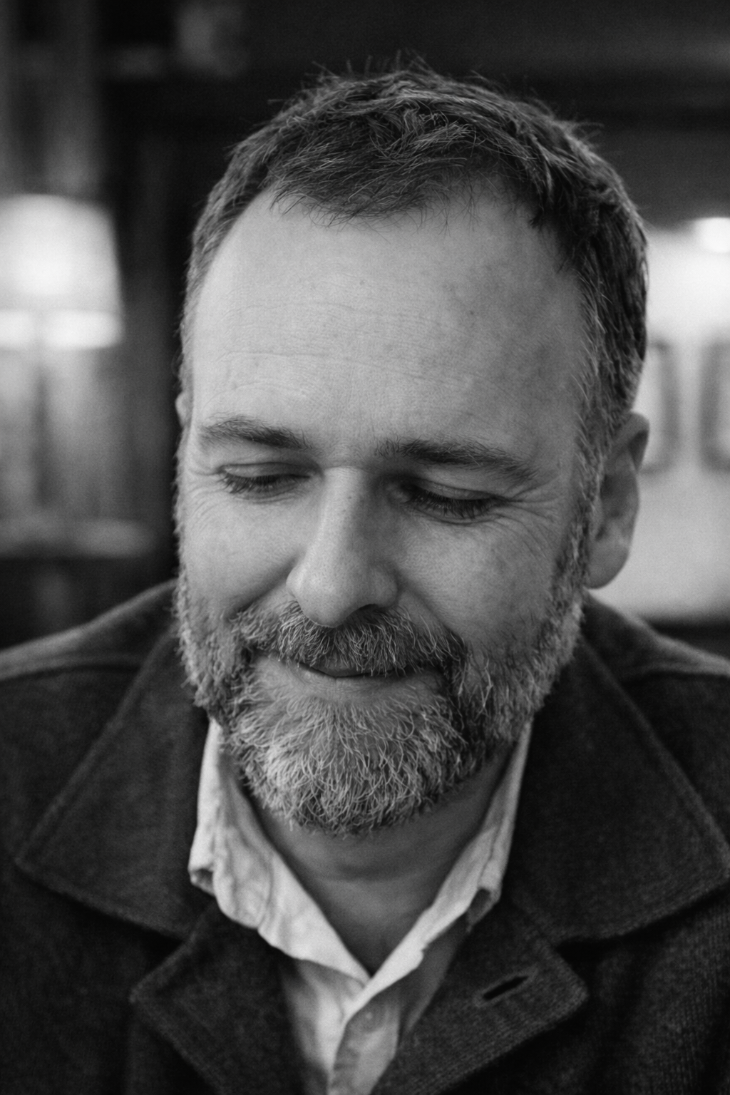Un homme avec une barbe et des cheveux courts, souriant avec les yeux fermés, en noir et blanc.