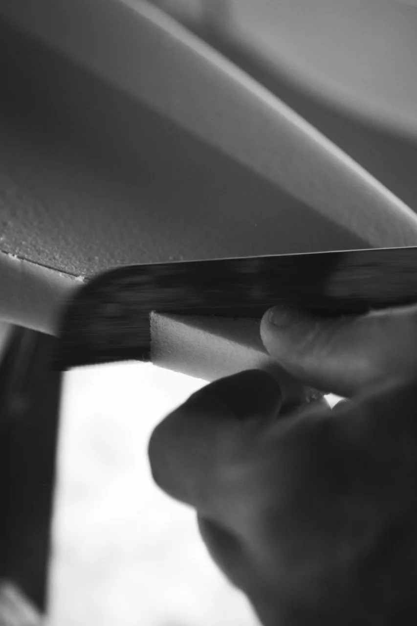 Nahaufnahme einer Hand, die ein Schaummaterial mit einem Sägewerkzeug schneidet.