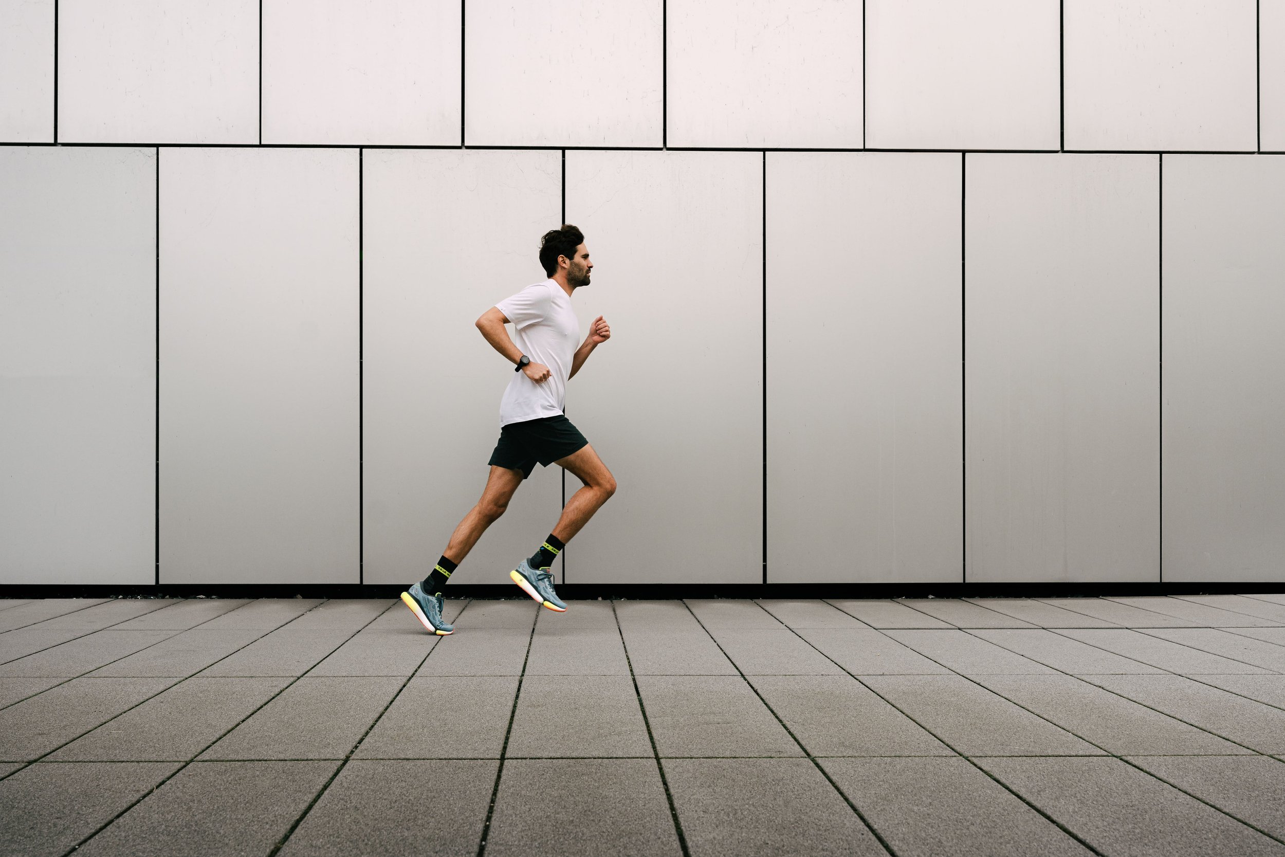 Ein Mann in Sportbekleidung joggt entlang einer modernen Gebäudeoberfläche.
