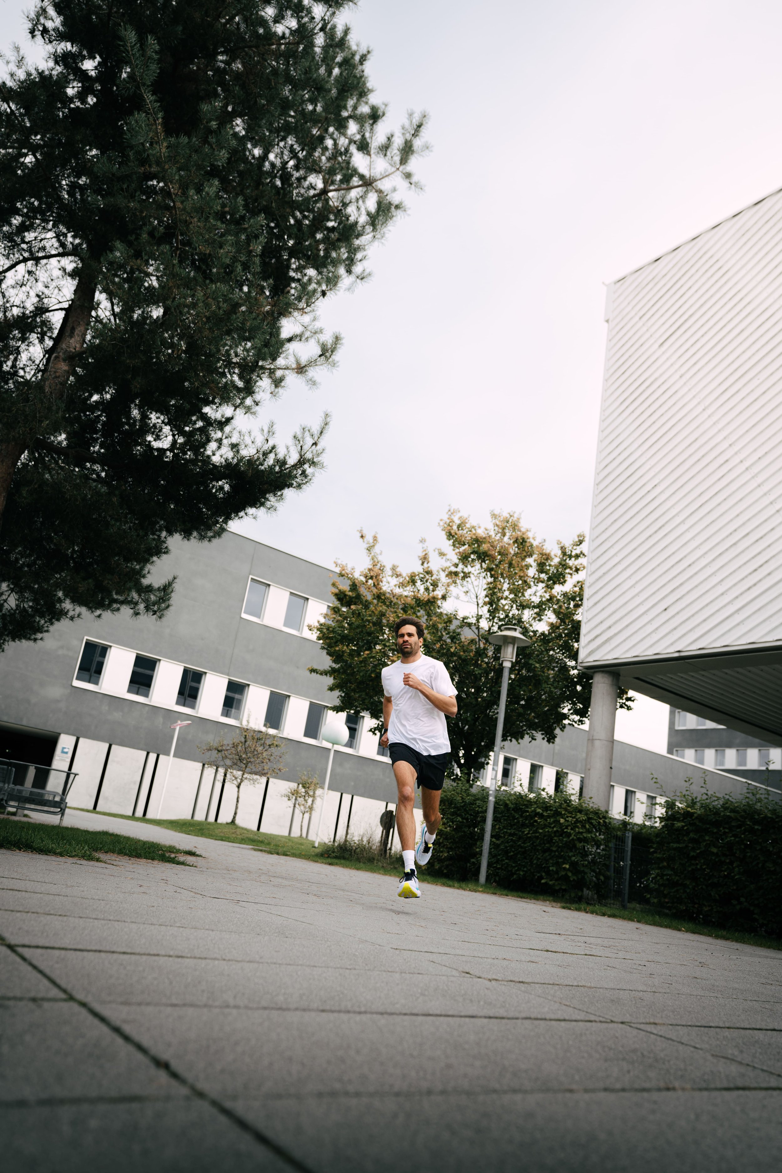 Mann joggt im Freien auf einem Gehweg. Im Hintergrund sind moderne Gebäude und Bäume zu sehen.