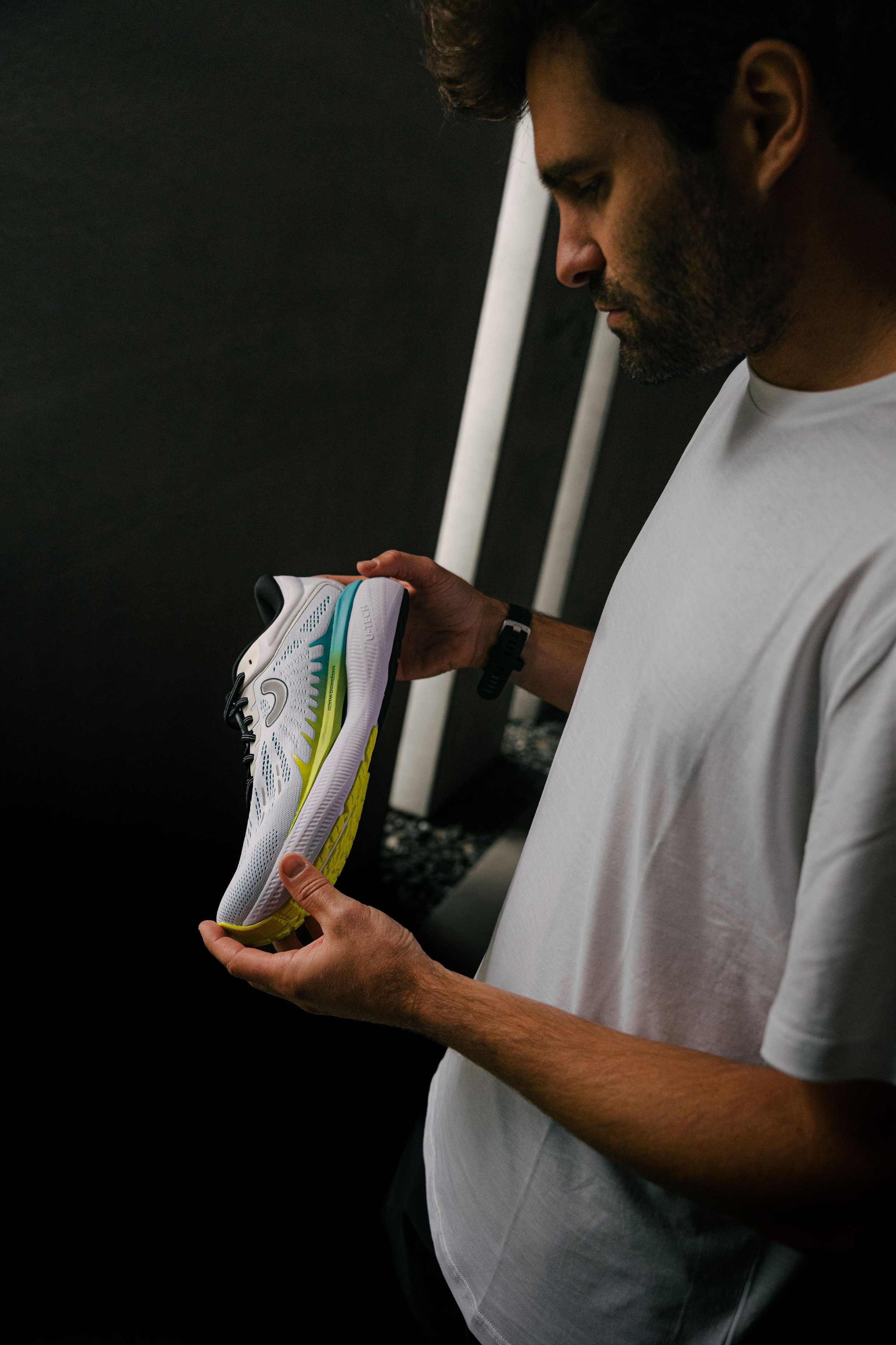 Mann hält einen weißen Sportschuh mit leuchtend gelber Sohle in den Händen, während er ein weißes T-Shirt trägt.