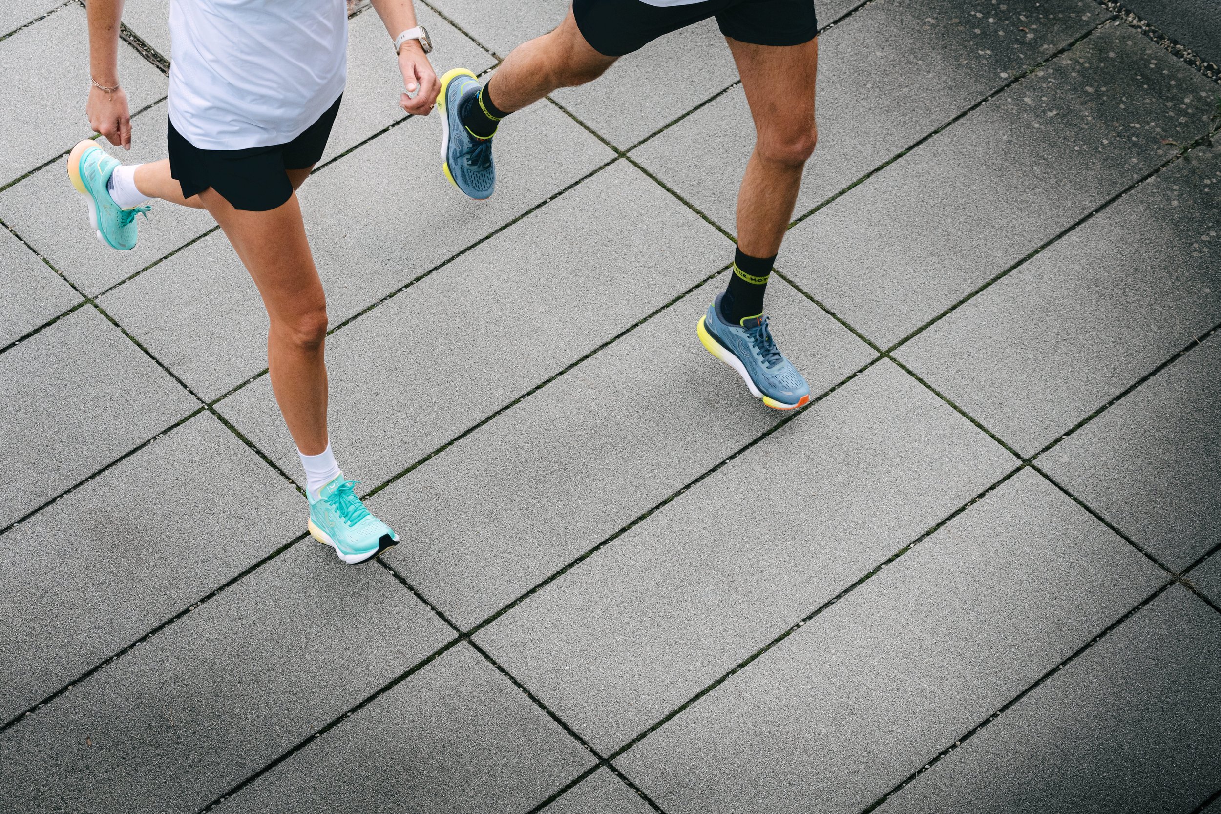 Zwei Personen rennen auf einem gepflasterten Weg, beide in Sportkleidung und Turnschuhen, von oben gesehen.