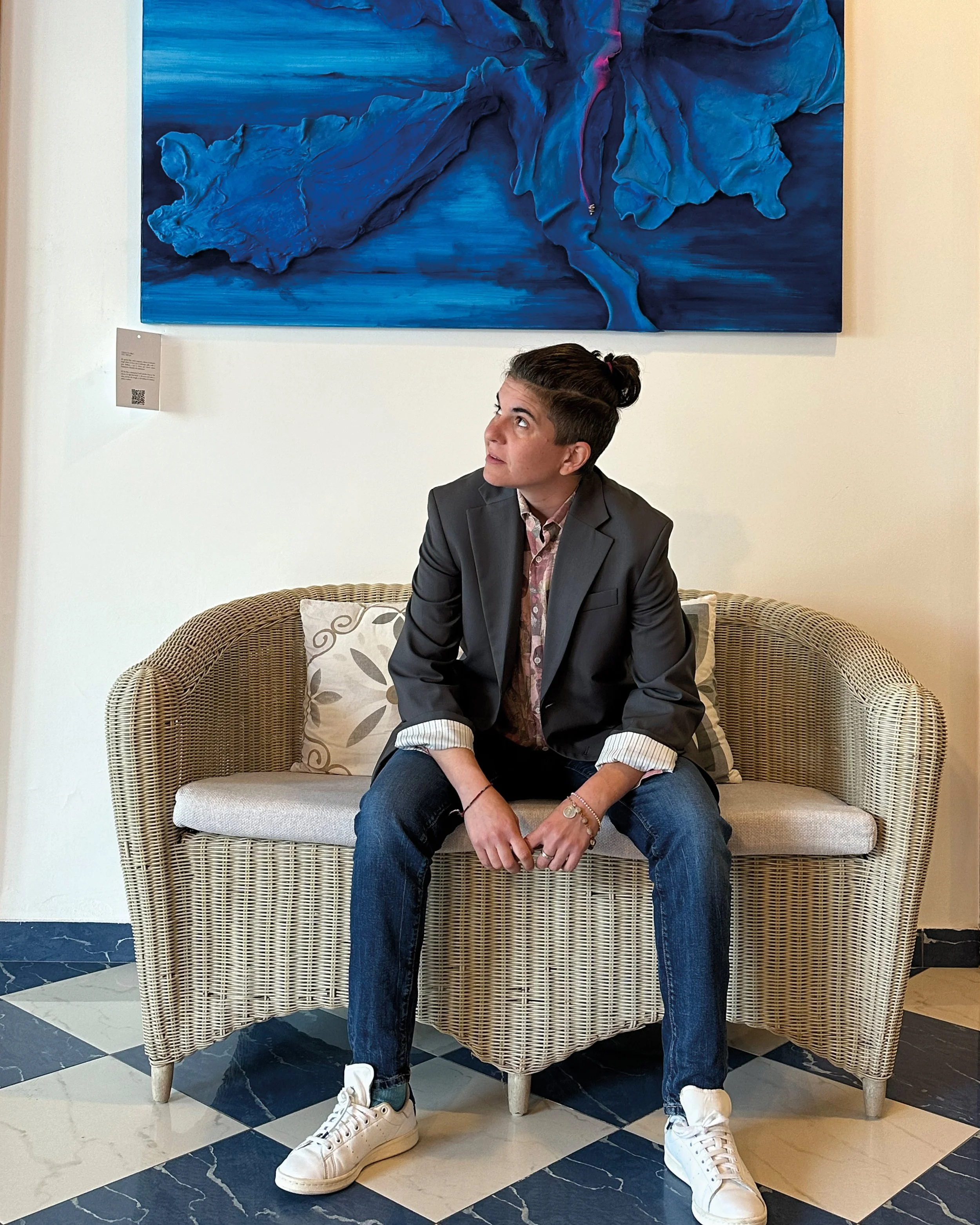 Retrato de la artista Vera Vizzi sentada bajo una de sus obras tridimensionales.