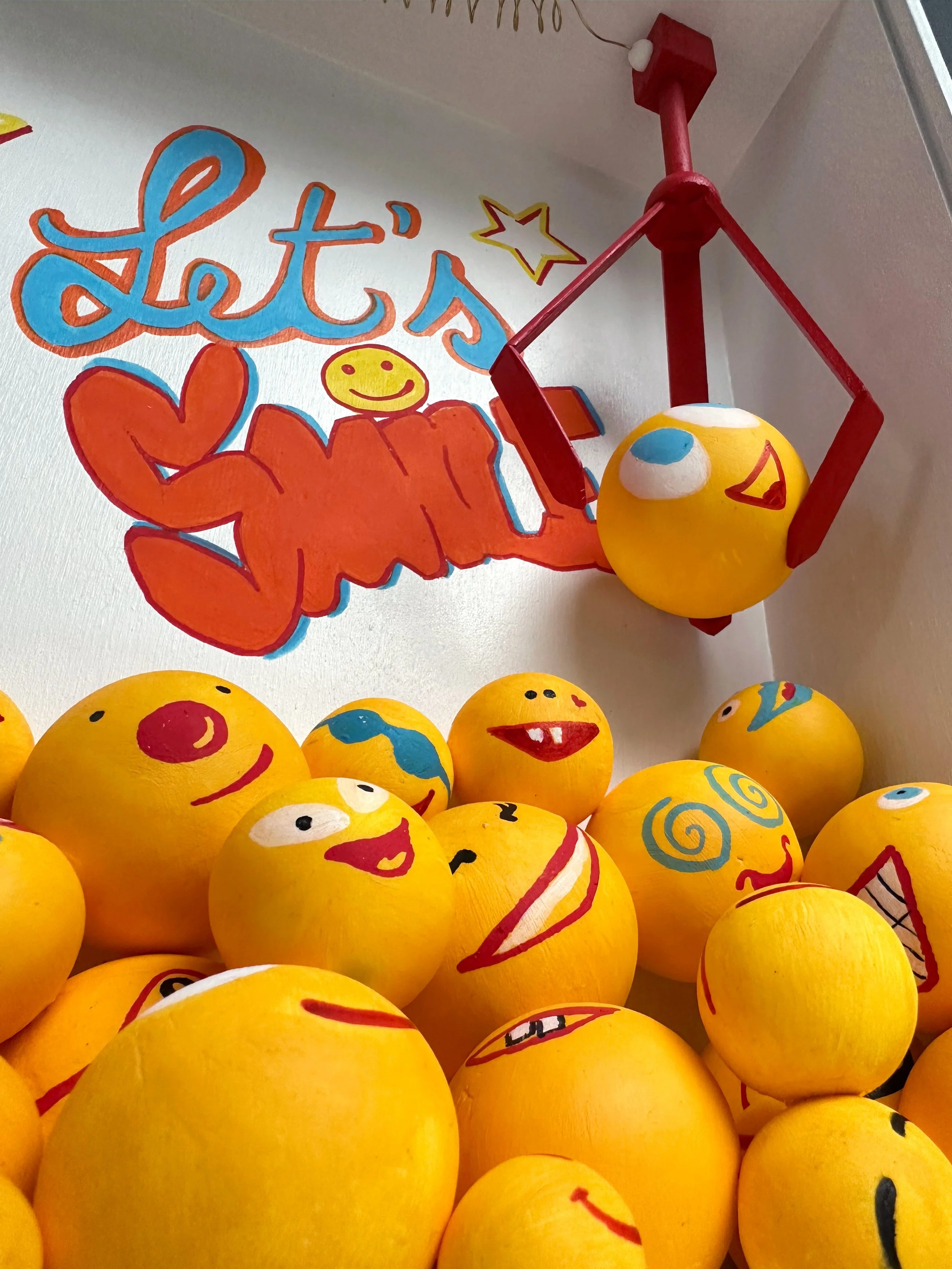 Detalle de la instalación Smile Machine, formada por figuras esféricas amarillas con diferentes expresiones.