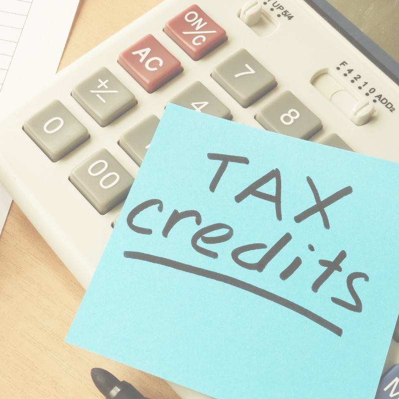 Close-up photo of a calculator with a blue sticky note on it that says 'TAX credits' in black handwritten letters.