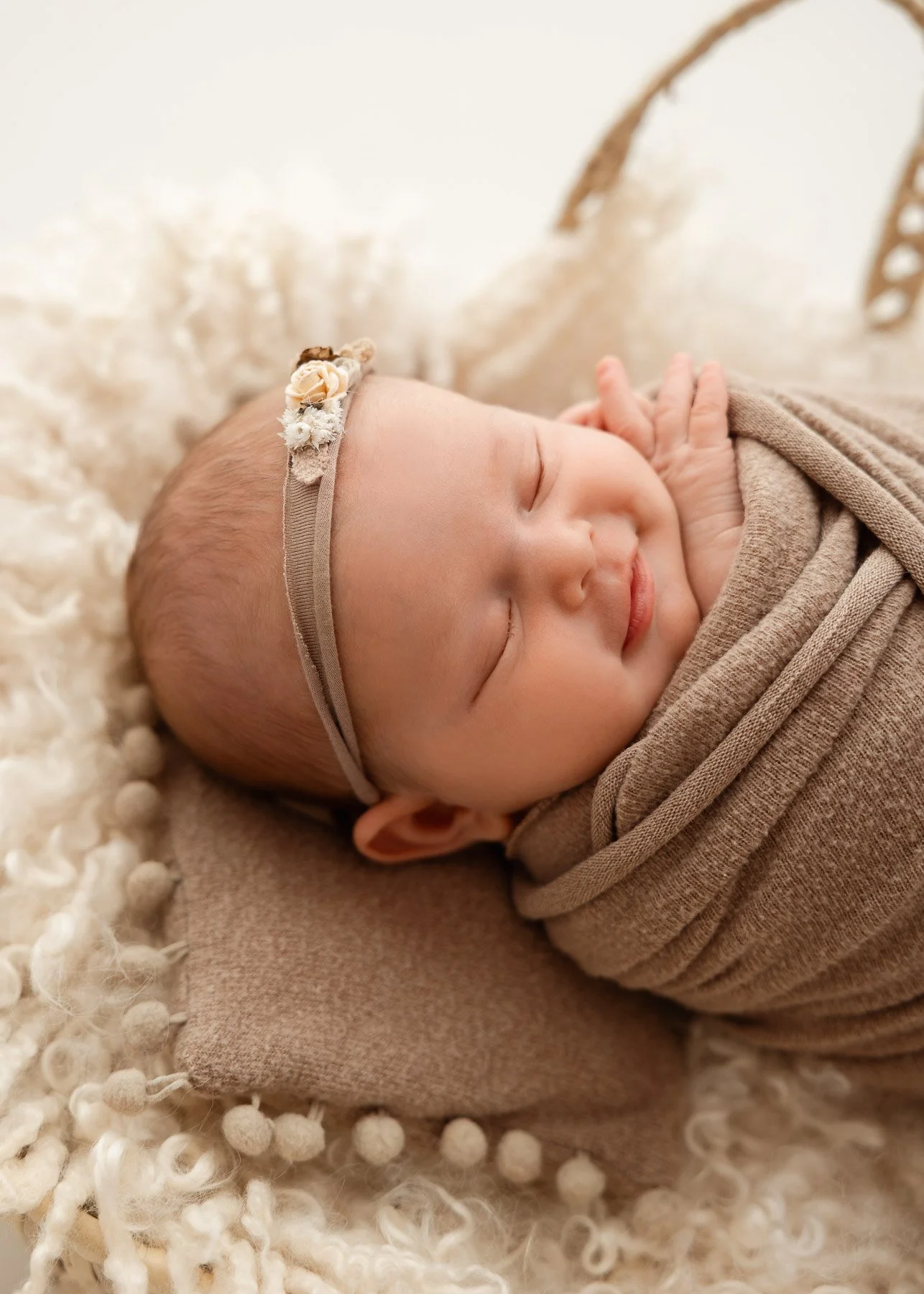 Ein schlafendes Baby mit einem Blumen-Haarband, eingebettet in eine weiche, cremefarbene Decke.