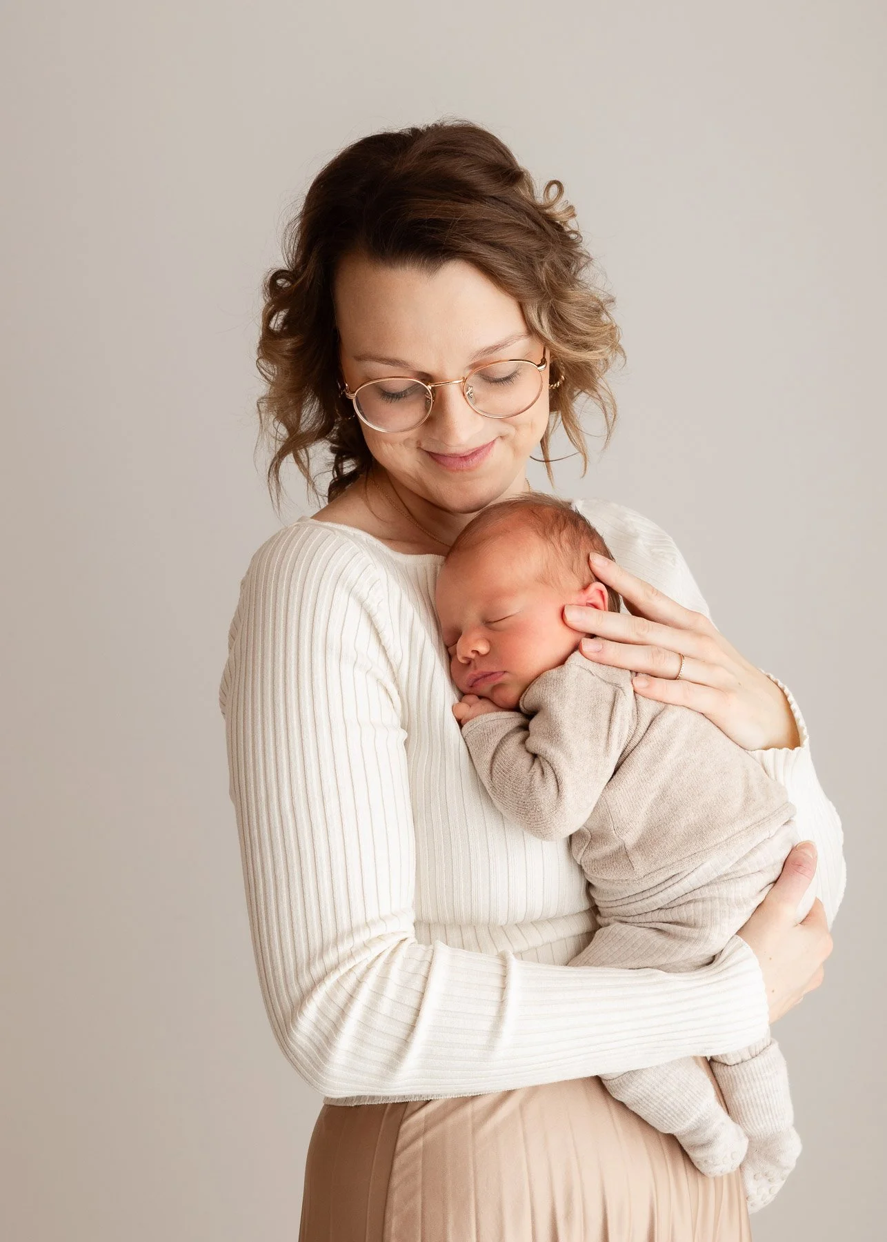 Eine Frau mit Brille hält ein schlafendes Baby, das sie liebevoll an sich gedrückt hat.