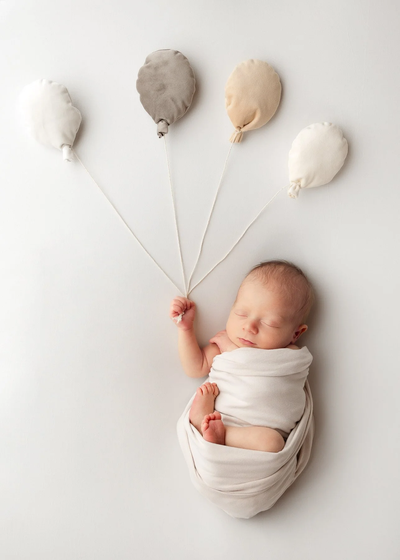 Schlafendes neugeborenes Baby in Decke eingewickelt, hält Schnüre von vier Stoffballons.
