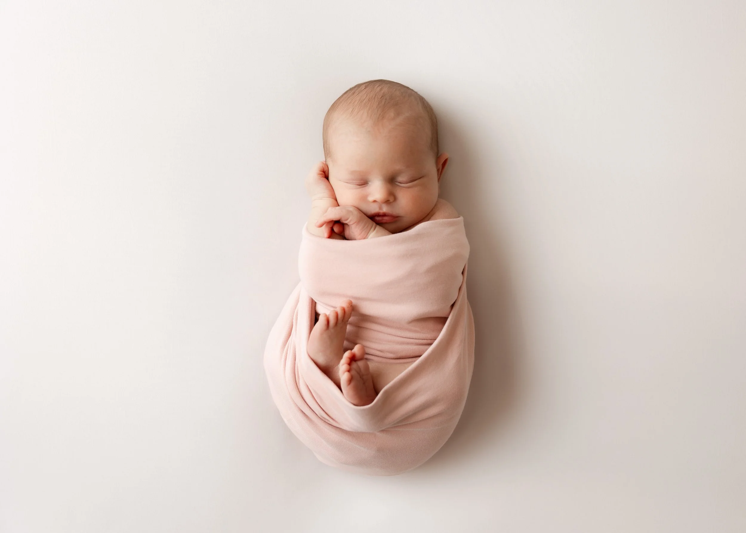 Ein neugeborenes Baby ist in einem rosafarbenen Tuch eingewickelt, schläft friedlich auf einem weißen Hintergrund.