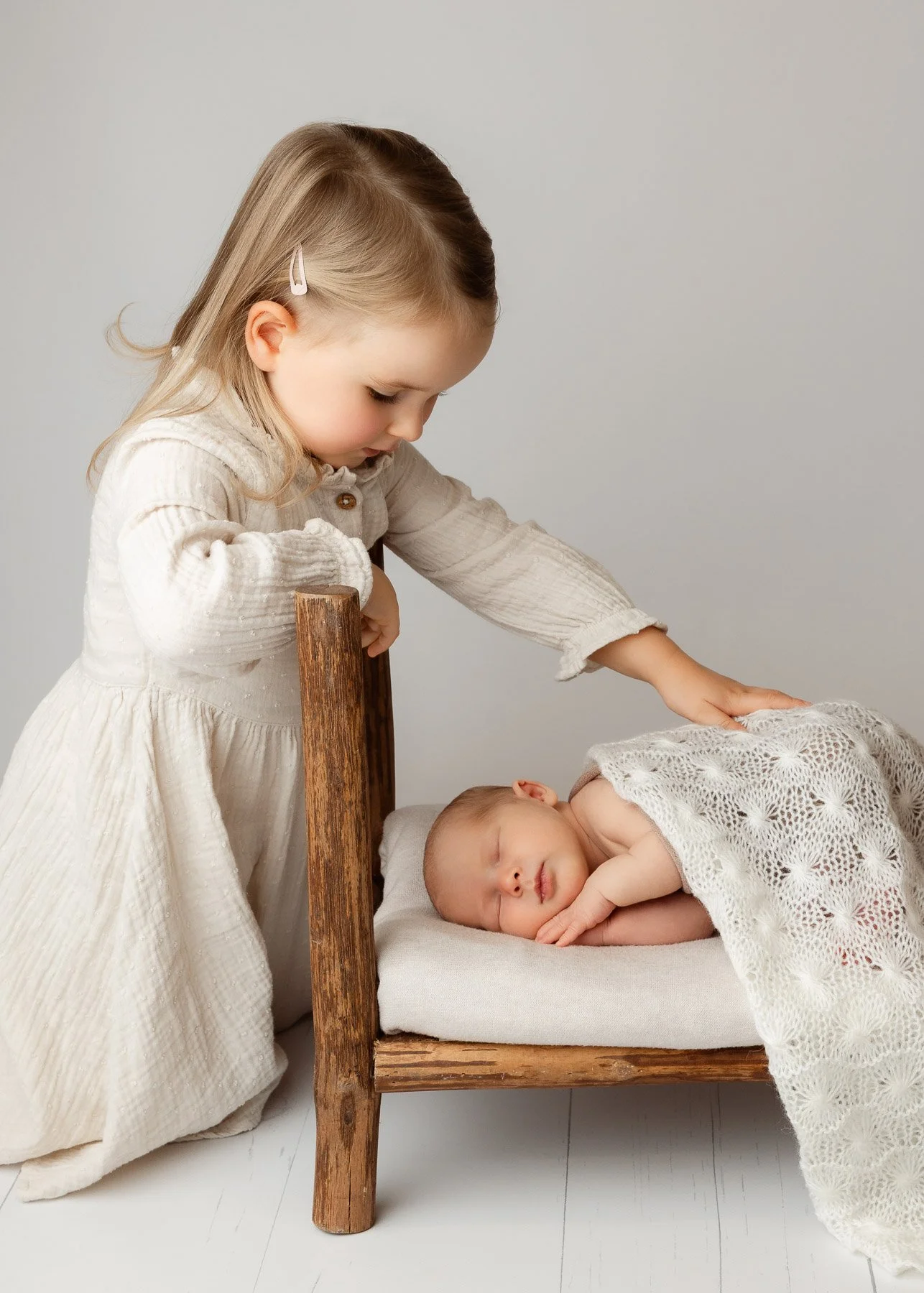 Ein kleines Mädchen, das eine schlafende Baby auf einem kleinen Bett berührt.