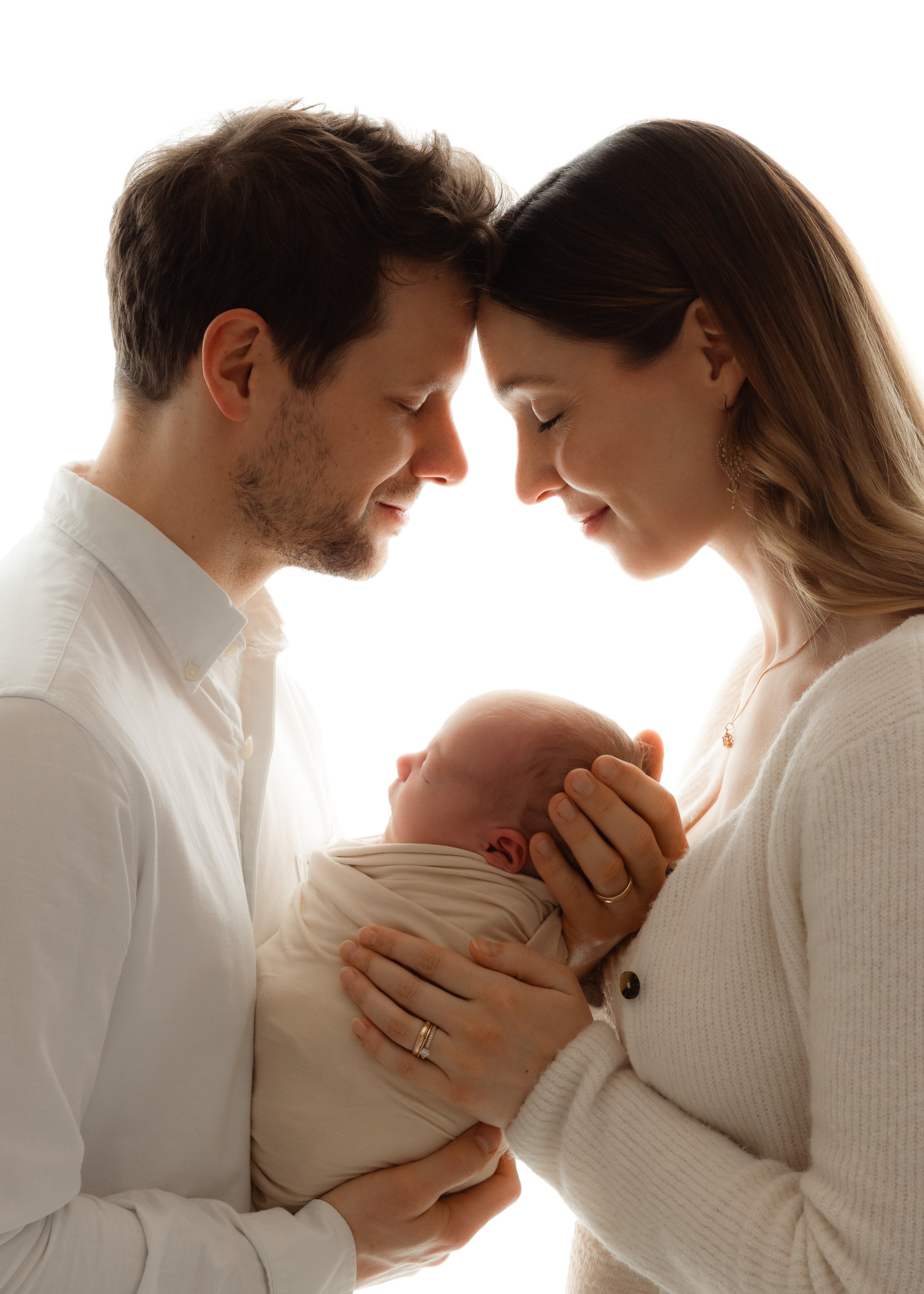 Ein Mann und eine Frau halten ein Baby gemeinsam und berühren ihre Stirnen, wobei ihre Augen geschlossen sind.
