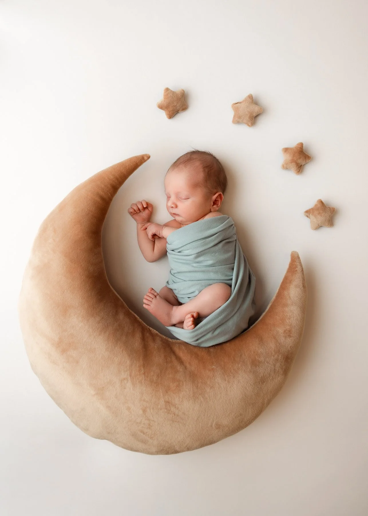 Ein schlafender Säugling liegt auf einem Mondkissen mit Sternen herum, alles auf einem weißen Hintergrund.