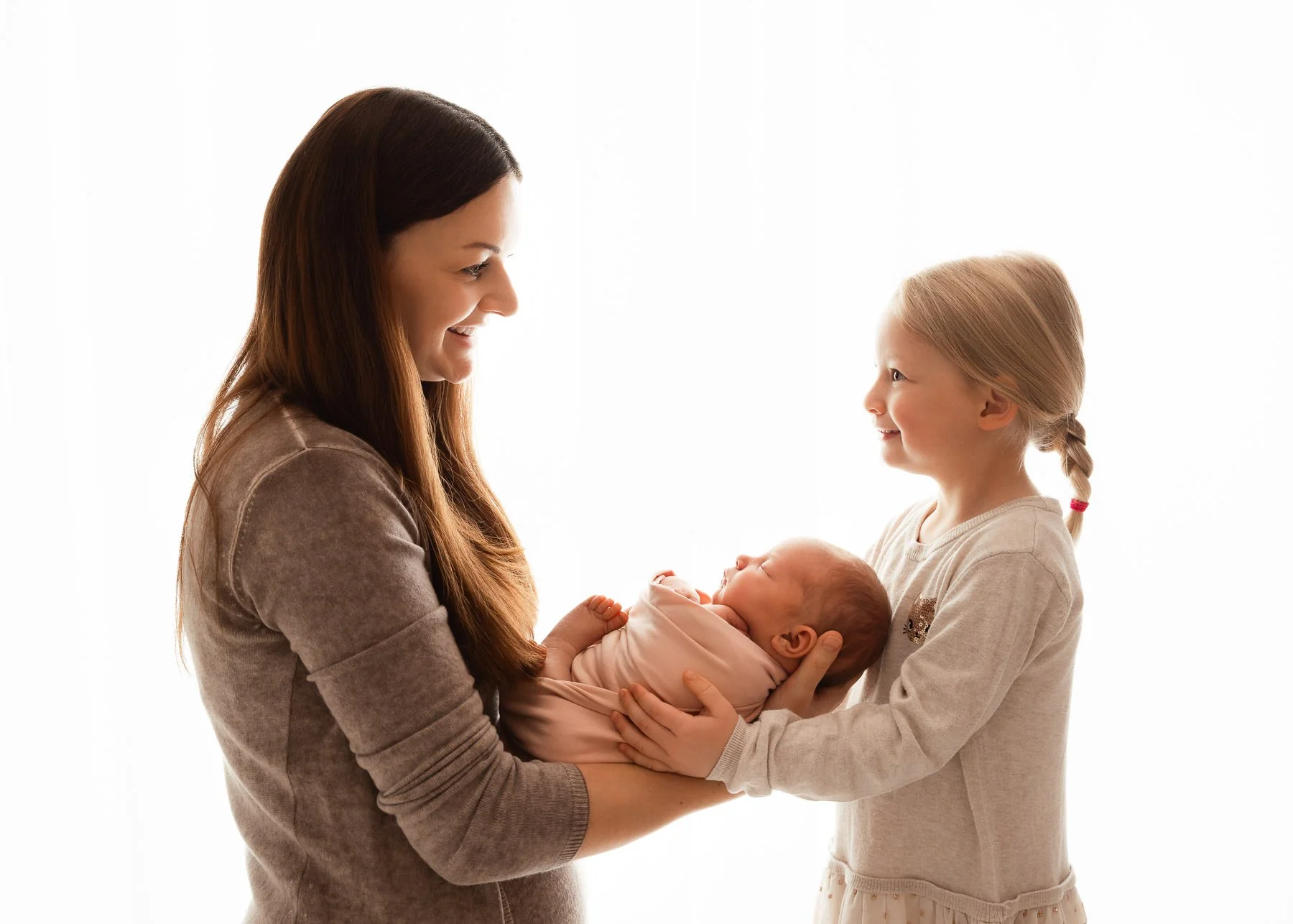 Eine Frau und ein kleines Mädchen halten gemeinsam ein Neugeborenes in einem Fotostudio.