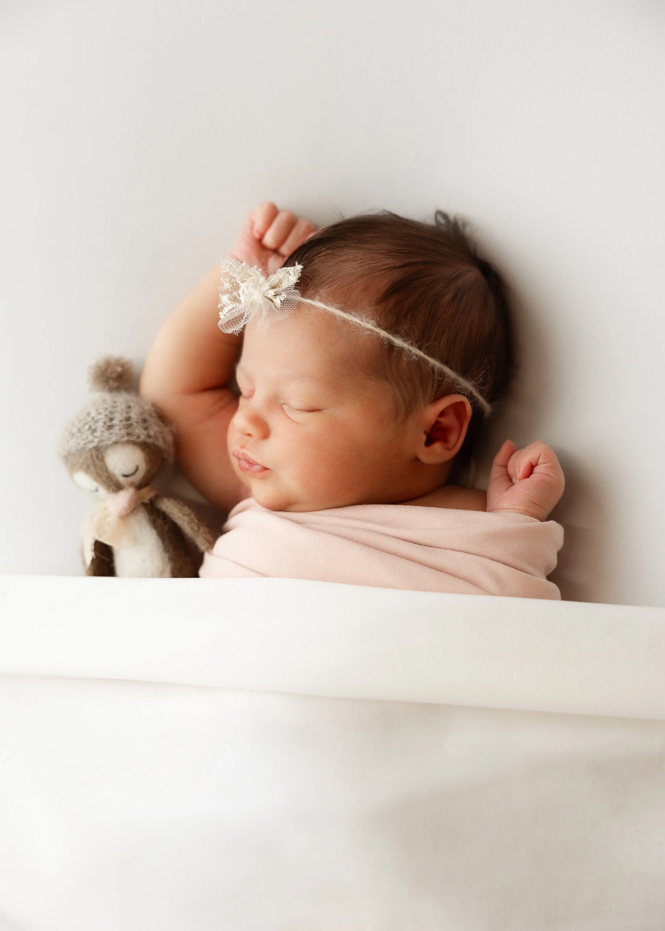 Ein schlafendes Baby, das in eine Decke gewickelt ist, mit einem Häkelspielzeug und einem Stirnband mit Schleife.