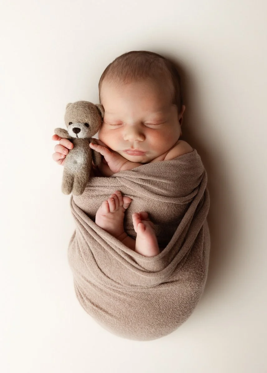 Schlafendes newborn Baby eingewickelt in braune Decke, hält kleinen Plüschbären.