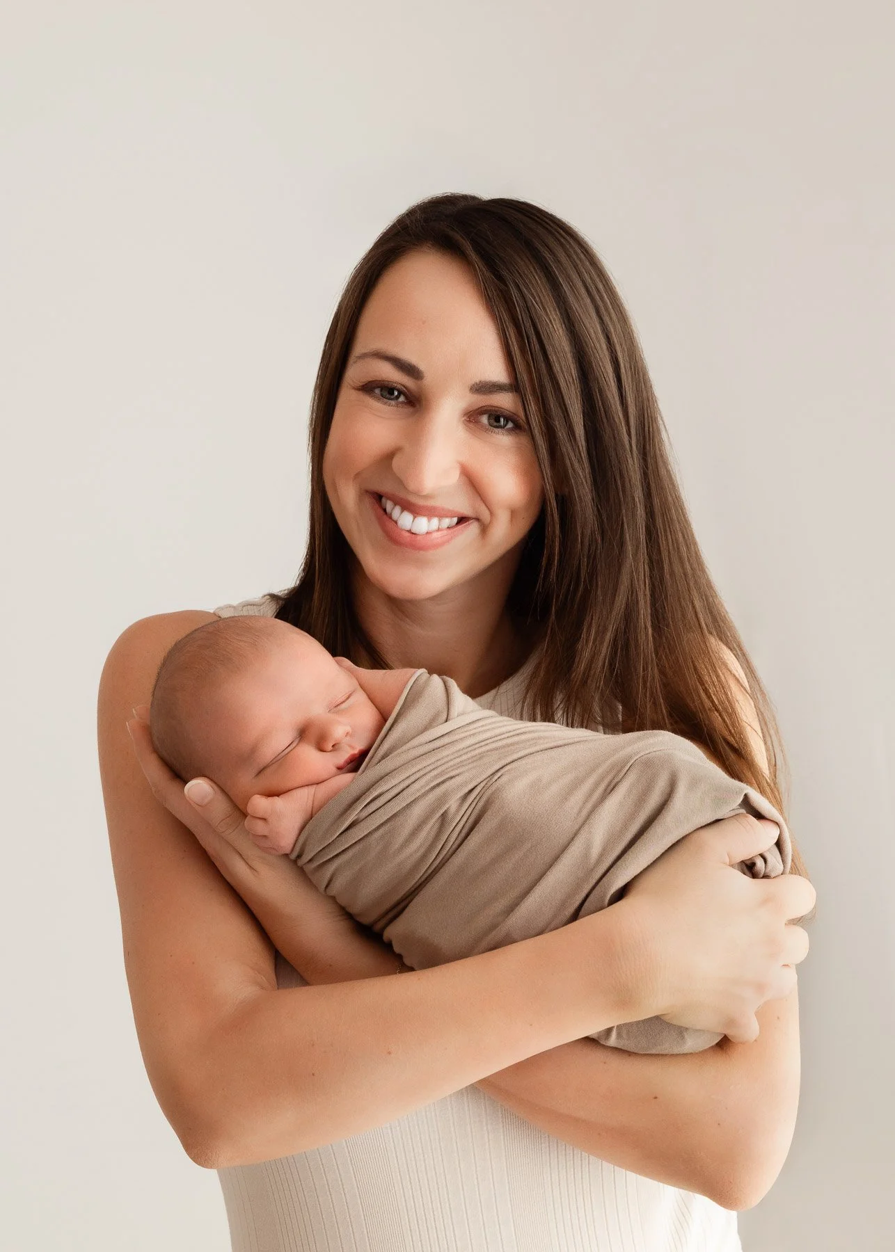 Eine lachende Frau hält ein schlafendes Baby, das in einen beige Verband gewickelt ist.