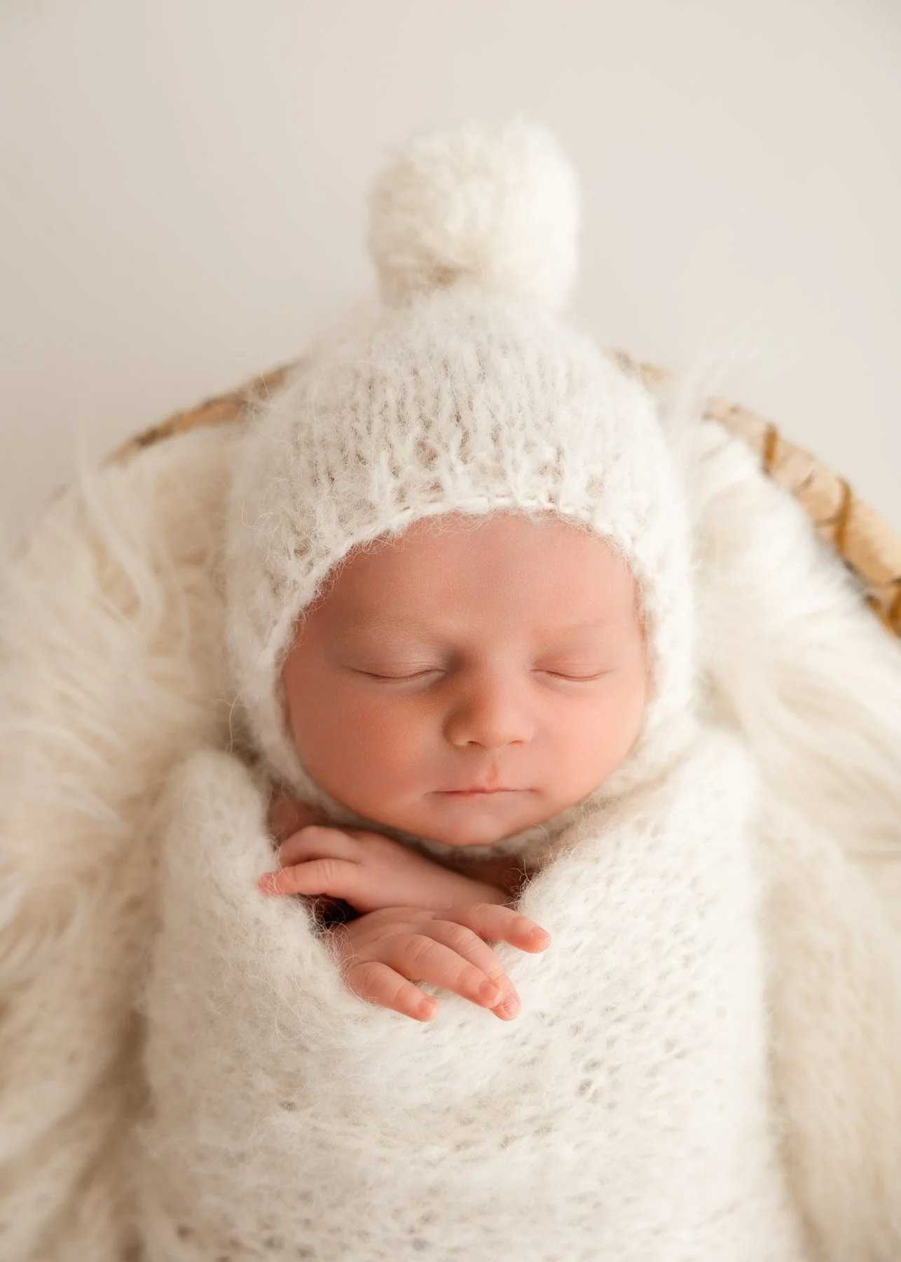 Ein schlafendes Baby eingewickelt in ein weiches, weißes Fell mit einem weißen, wolligen Mützchen.
