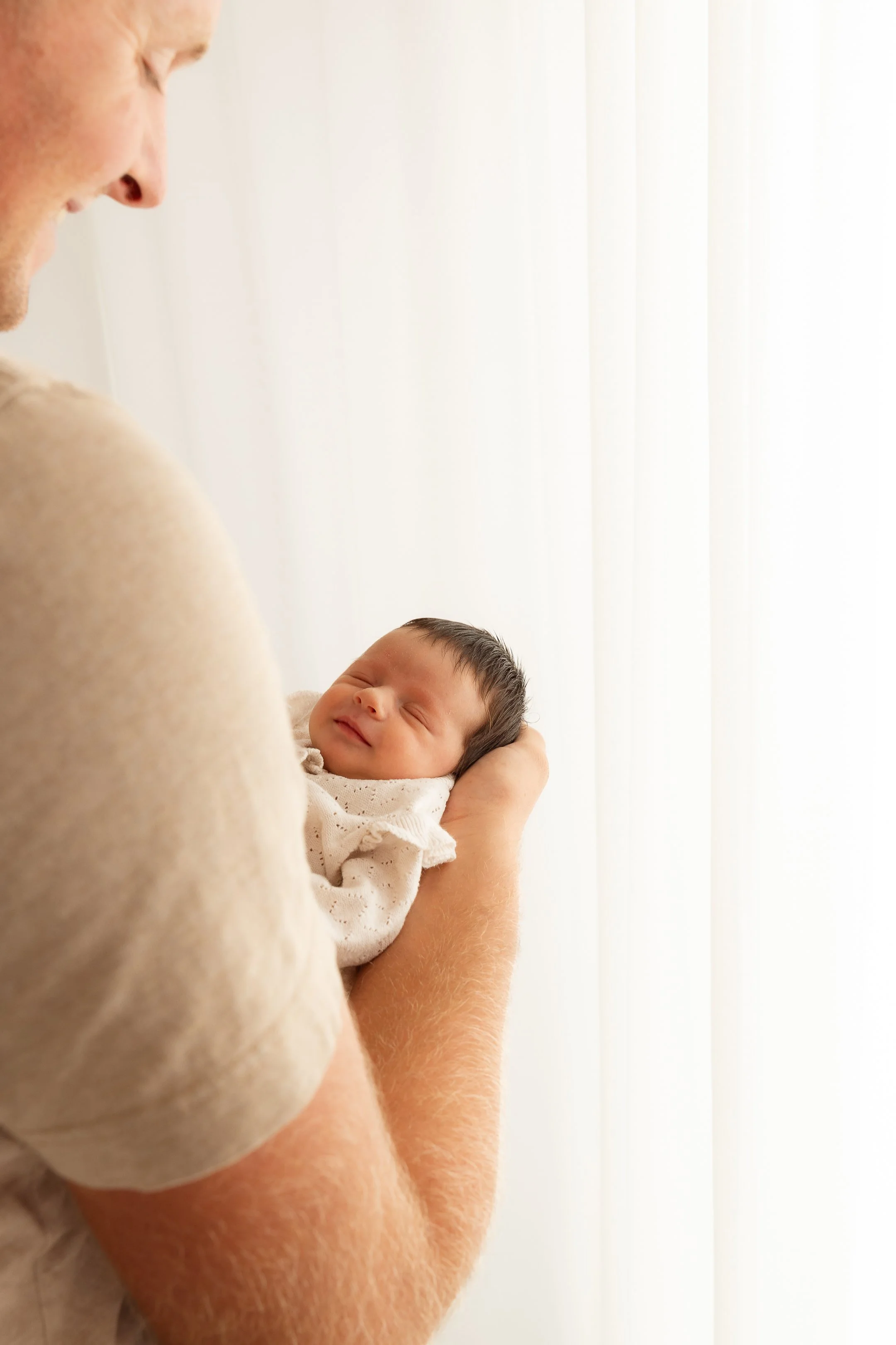 Ein Mann hält ein schlafendes Baby in den Armen, vor einem hell erleuchteten Vorhang