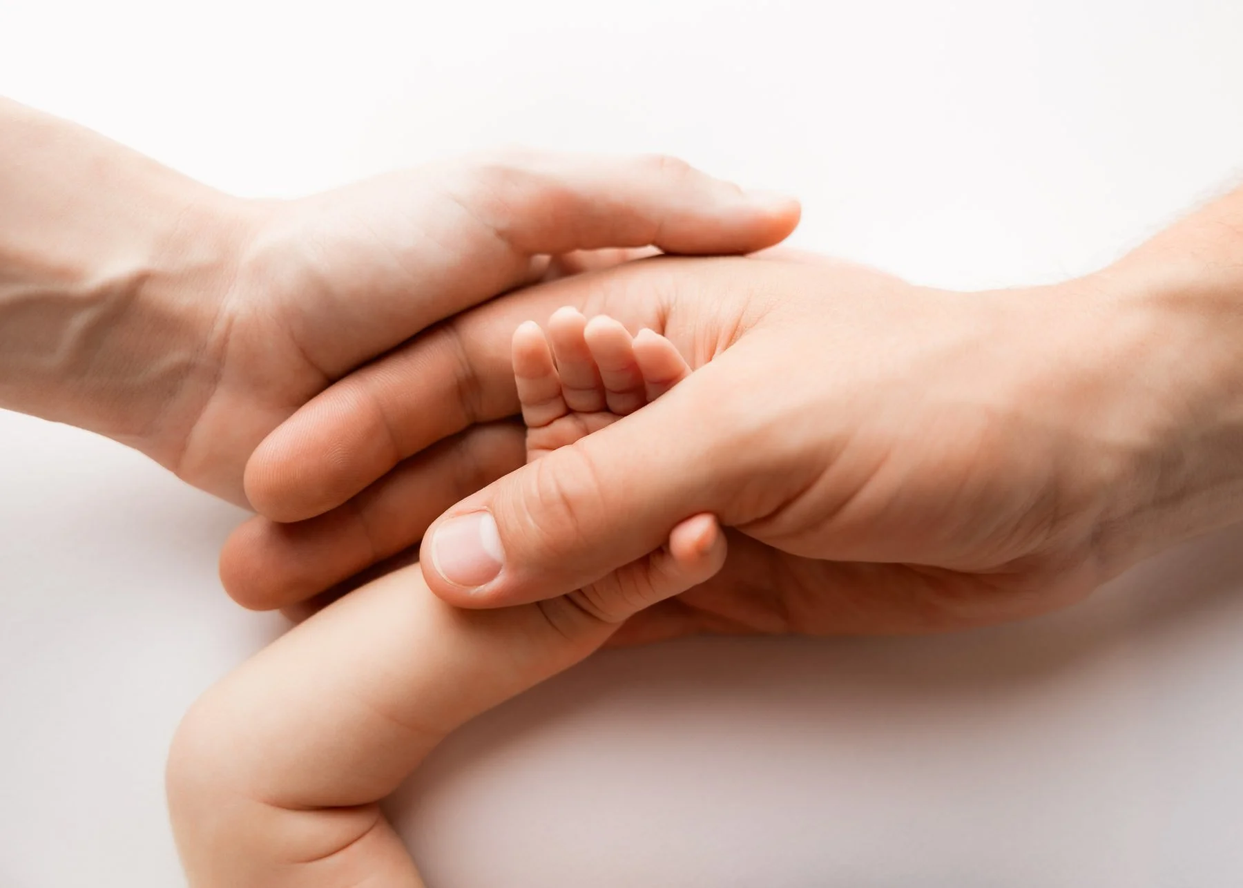 Zwei erwachsene Hände halten die kleine Hand eines Babys.