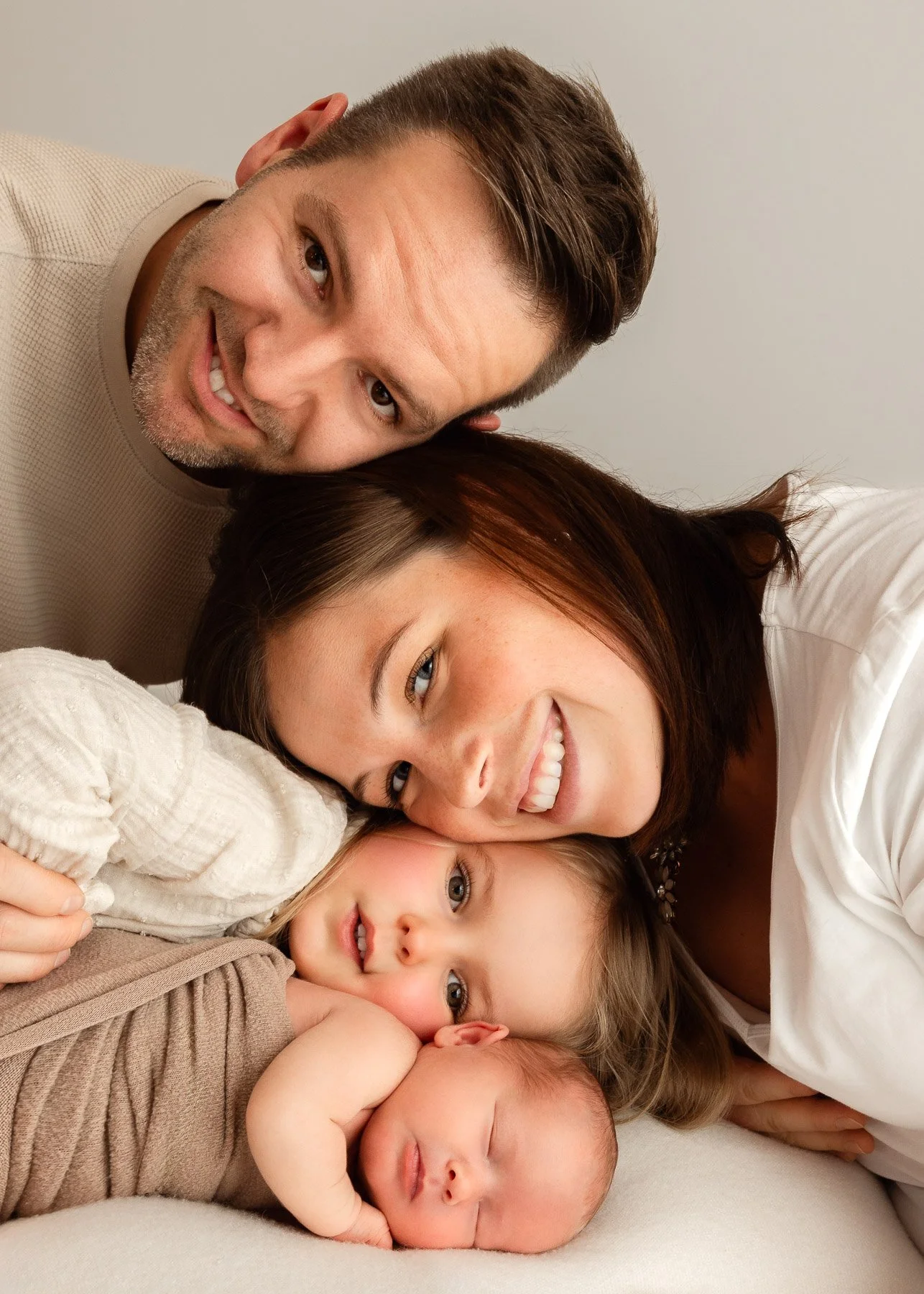 Familie mit zwei Kindern liegt zusammen auf einem Bett und lächelt.
