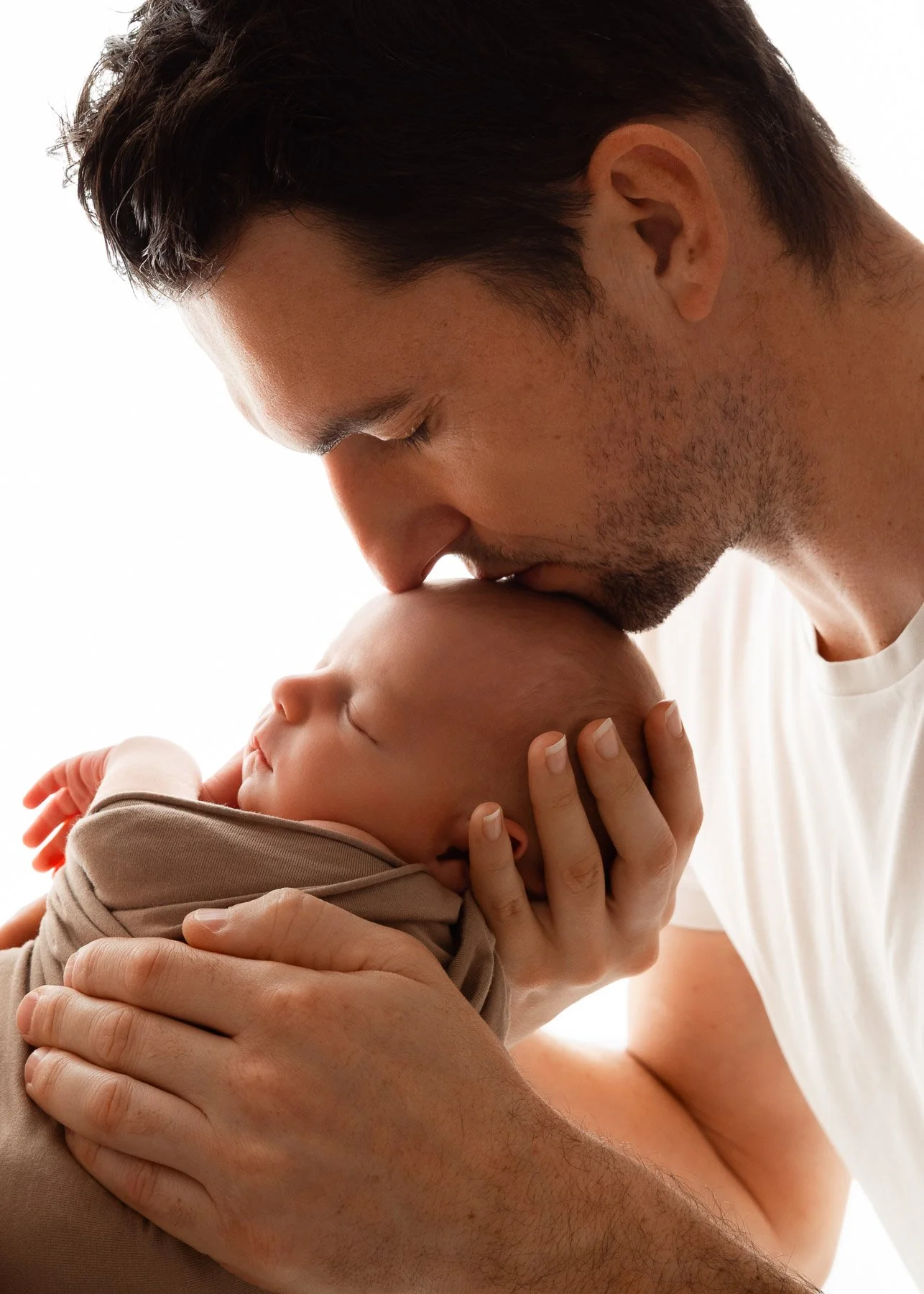 Vater küsst schlafendes Baby auf der Stirn. Nahaufnahme, liebevolle Zuneigung, Gefühl von Wärme und Geborgenheit.