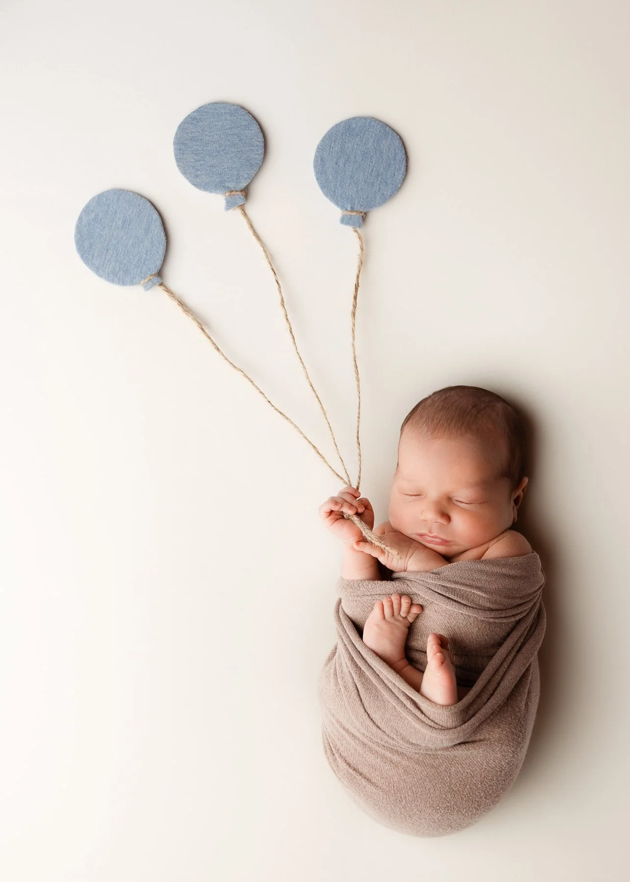 Ein schlafendes Baby in eine Decke gewickelt hält Schnüre, die zu drei blauen, runden Ballon-Dekorationen führen.