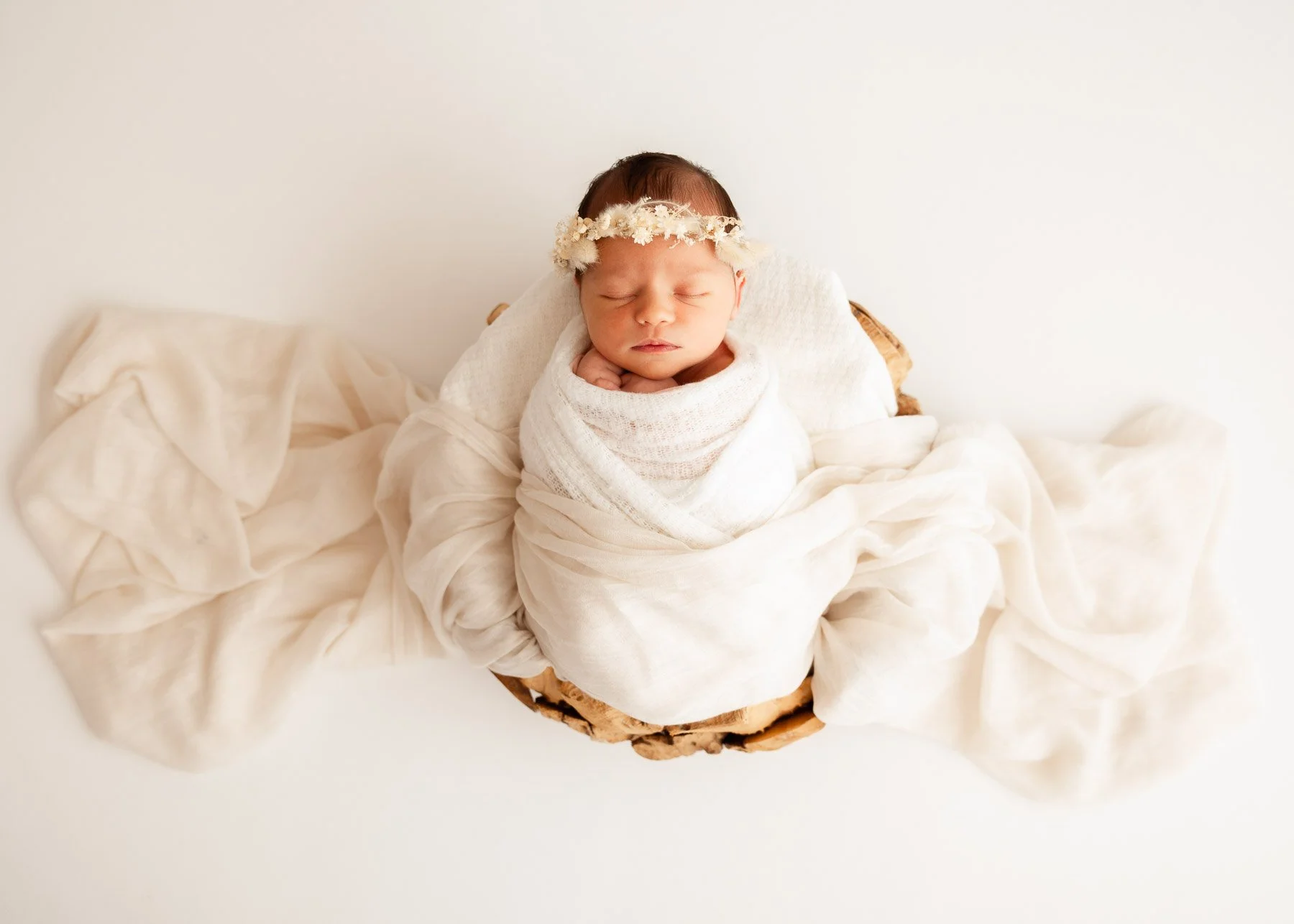 Schlafendes neugeborenes Baby in weißem Tuch gewickelt, mit Blumenstirnband, in einem Korb liegend.