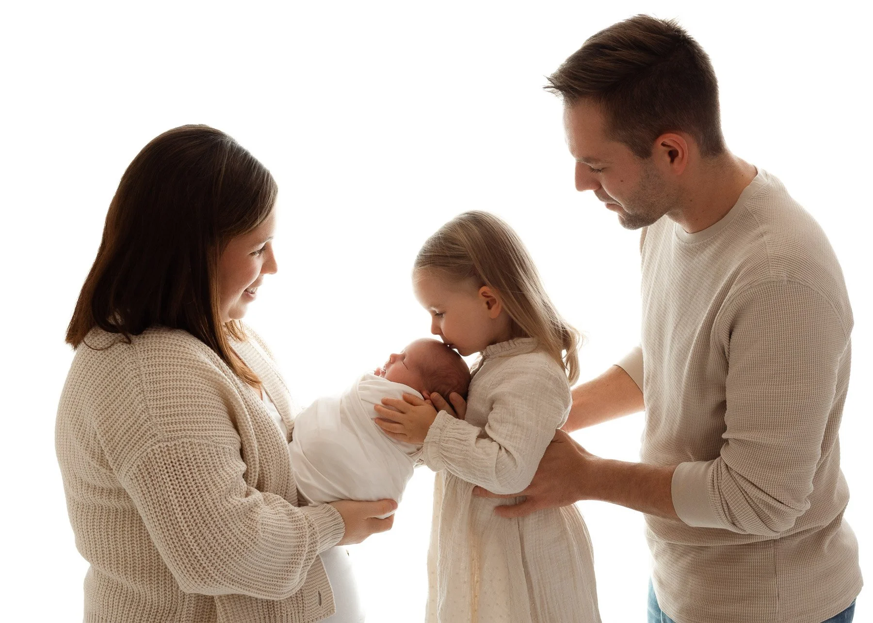 Familie mit zwei Kindern, ein Mädchen und ein Baby, das von der Mutter gehalten wird, während der Vater zuschaut, vor weißem Hintergrund.