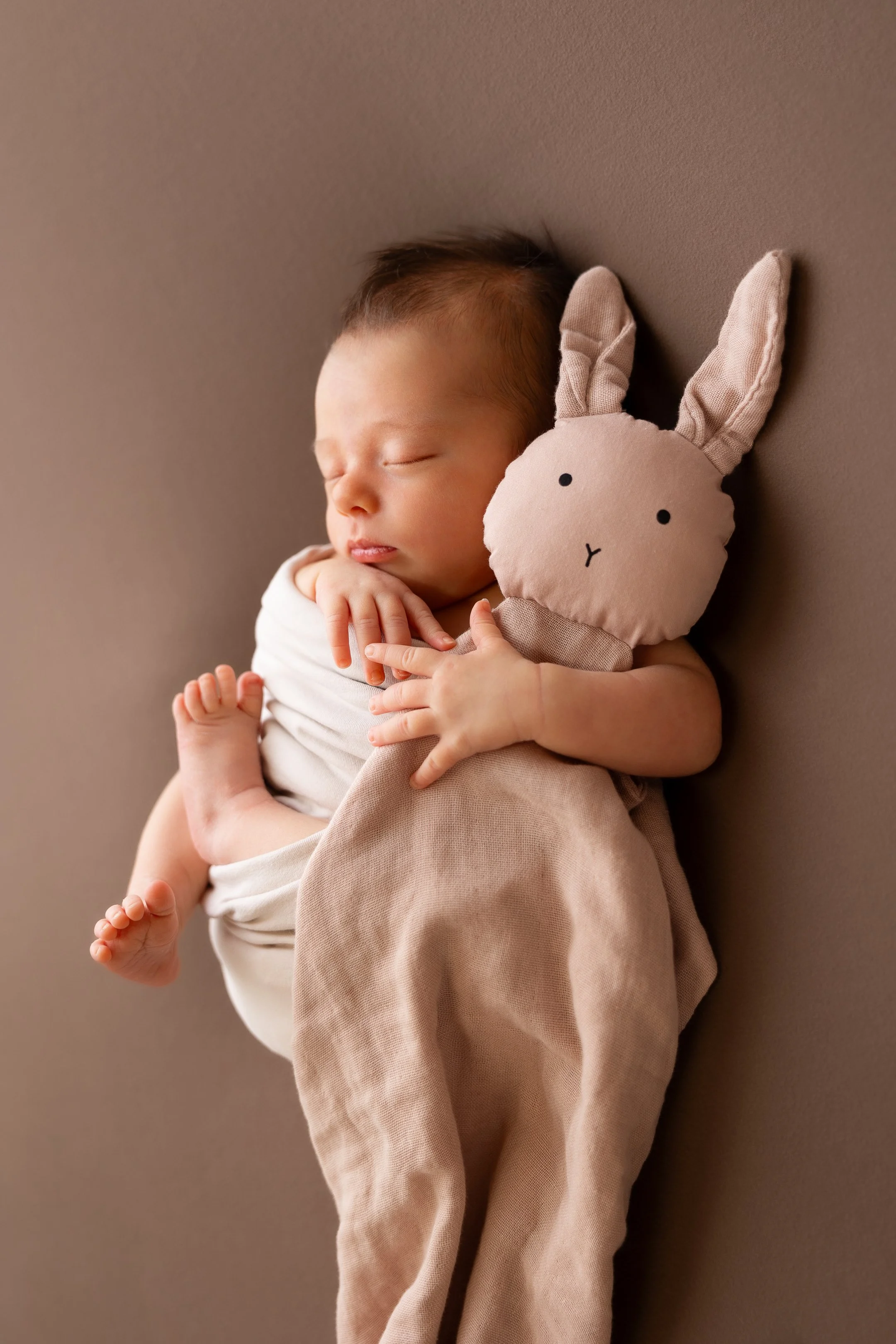 Schlafendes neugeborenes Baby in weißem Wickeltuch mit Stofftier