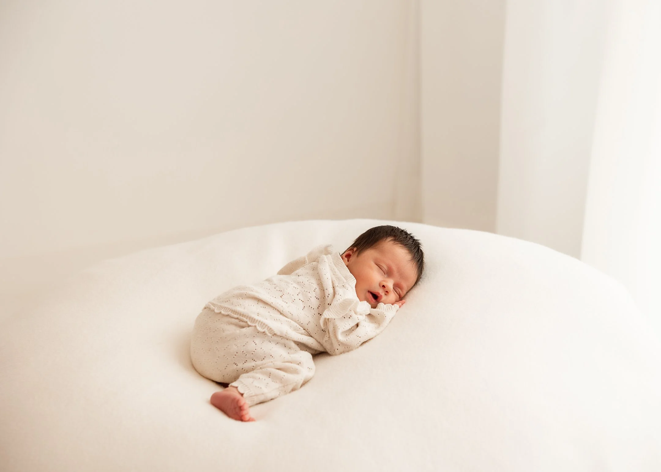 Ein neugeborenes Baby schläft auf einem weißen Bett, in einem hell erleuchteten Raum.