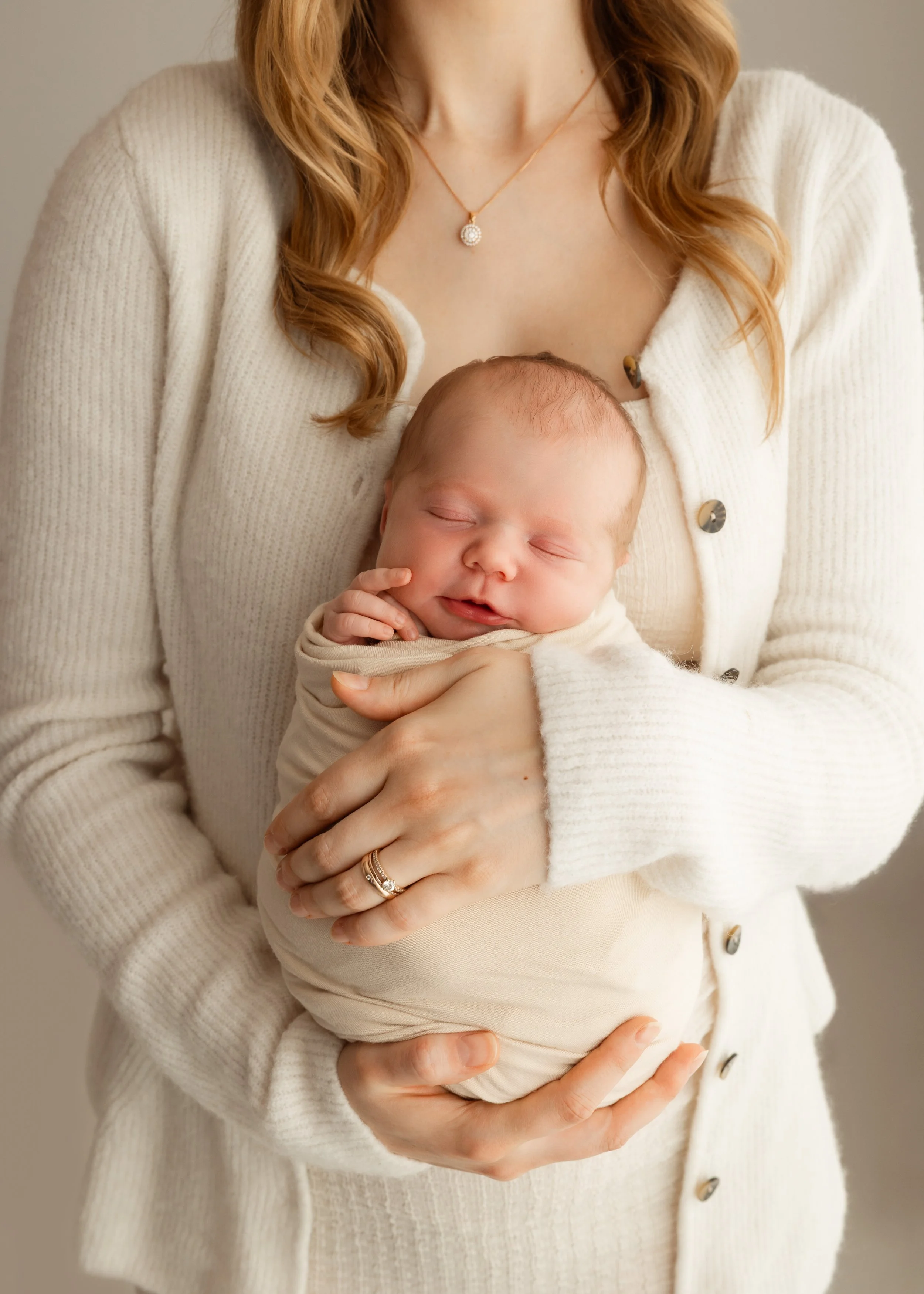 Eine Frau mit roten Haaren in einem weißen Pullover, die ein schlafendes Baby hält.