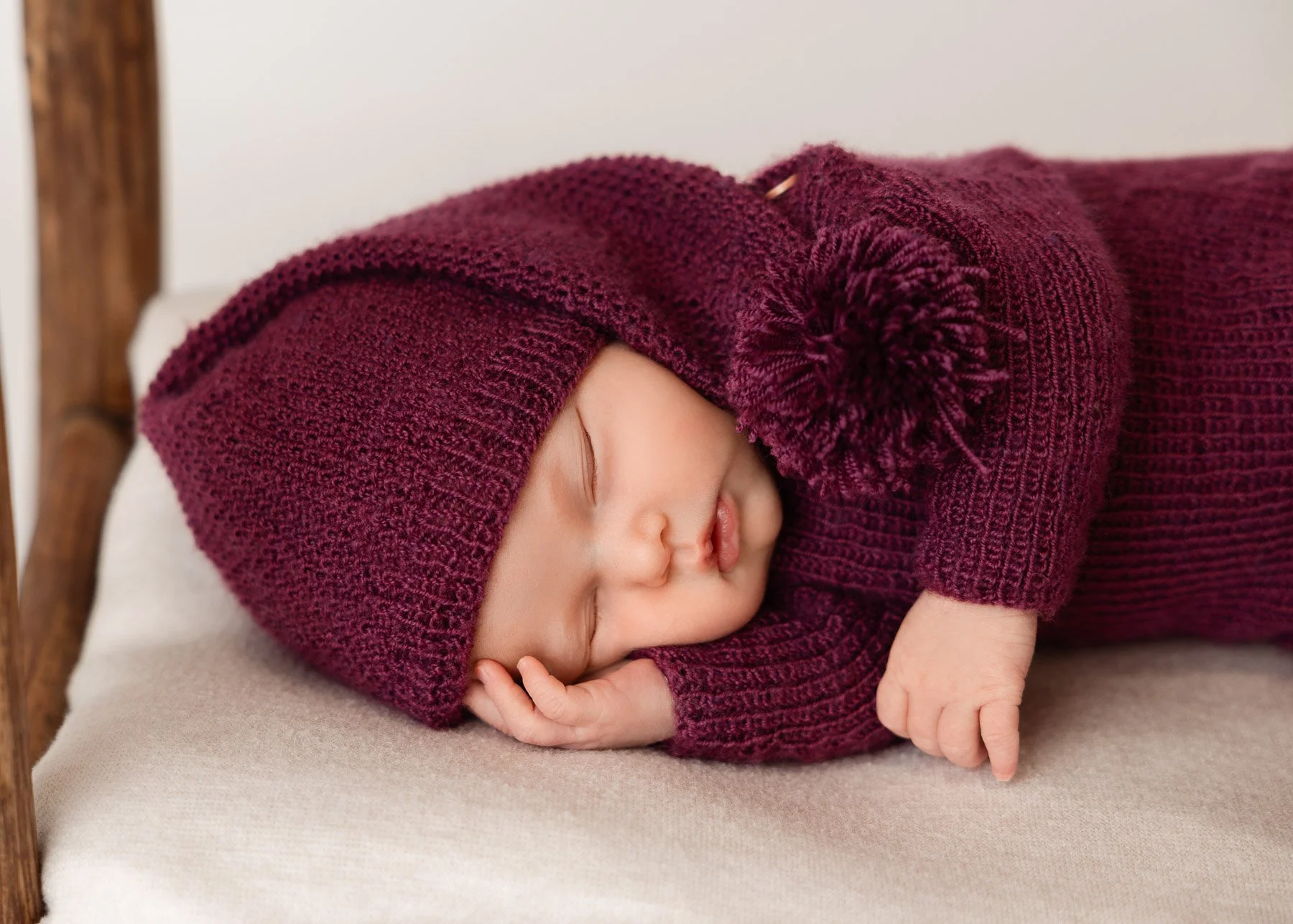 Ein schlafendes Baby in einem burgunderfarbenen Strickmütze und Pullover, liegend auf einem Bett.