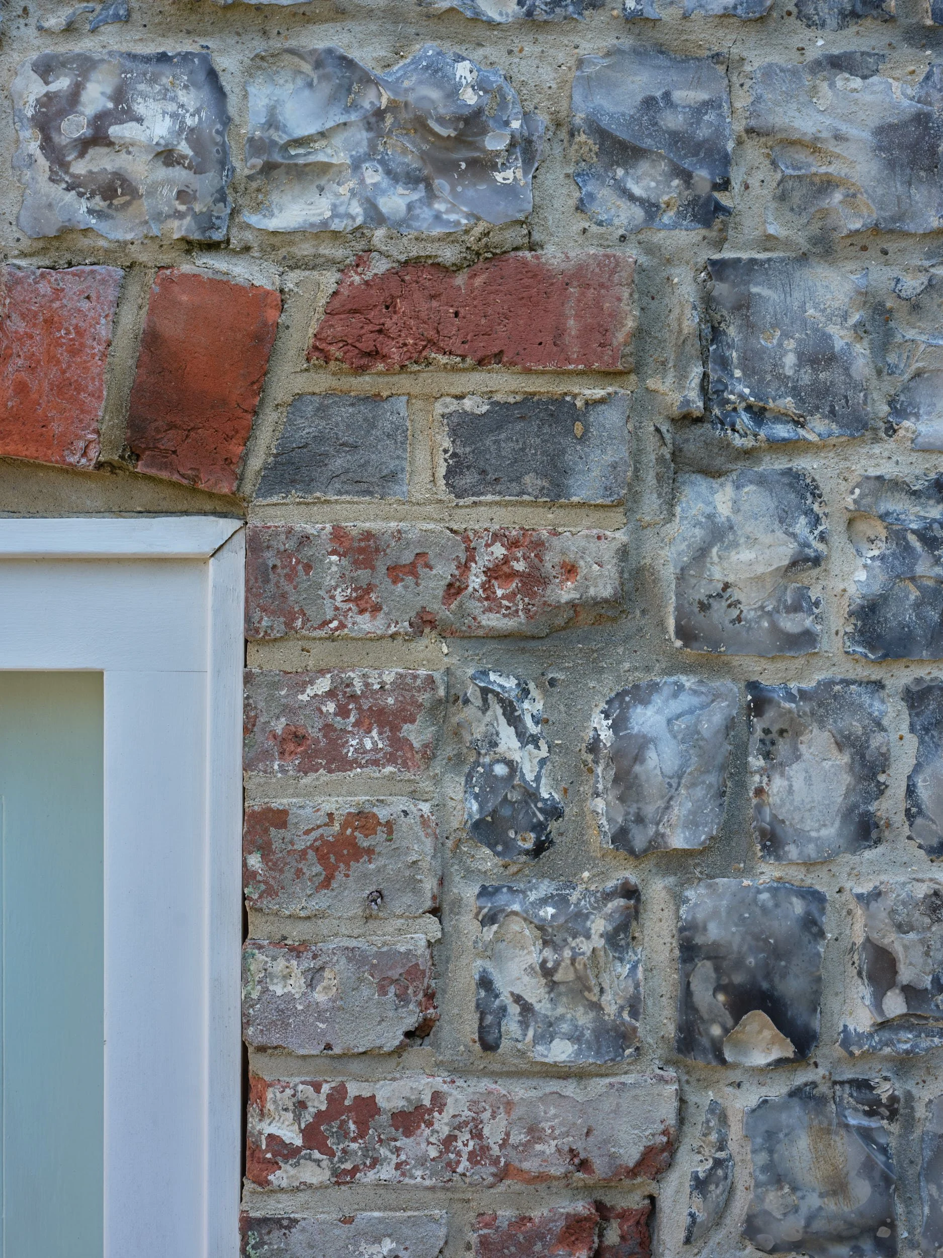 Close-up of brick and stone wall with part of a white window frame in the bottom left corner.