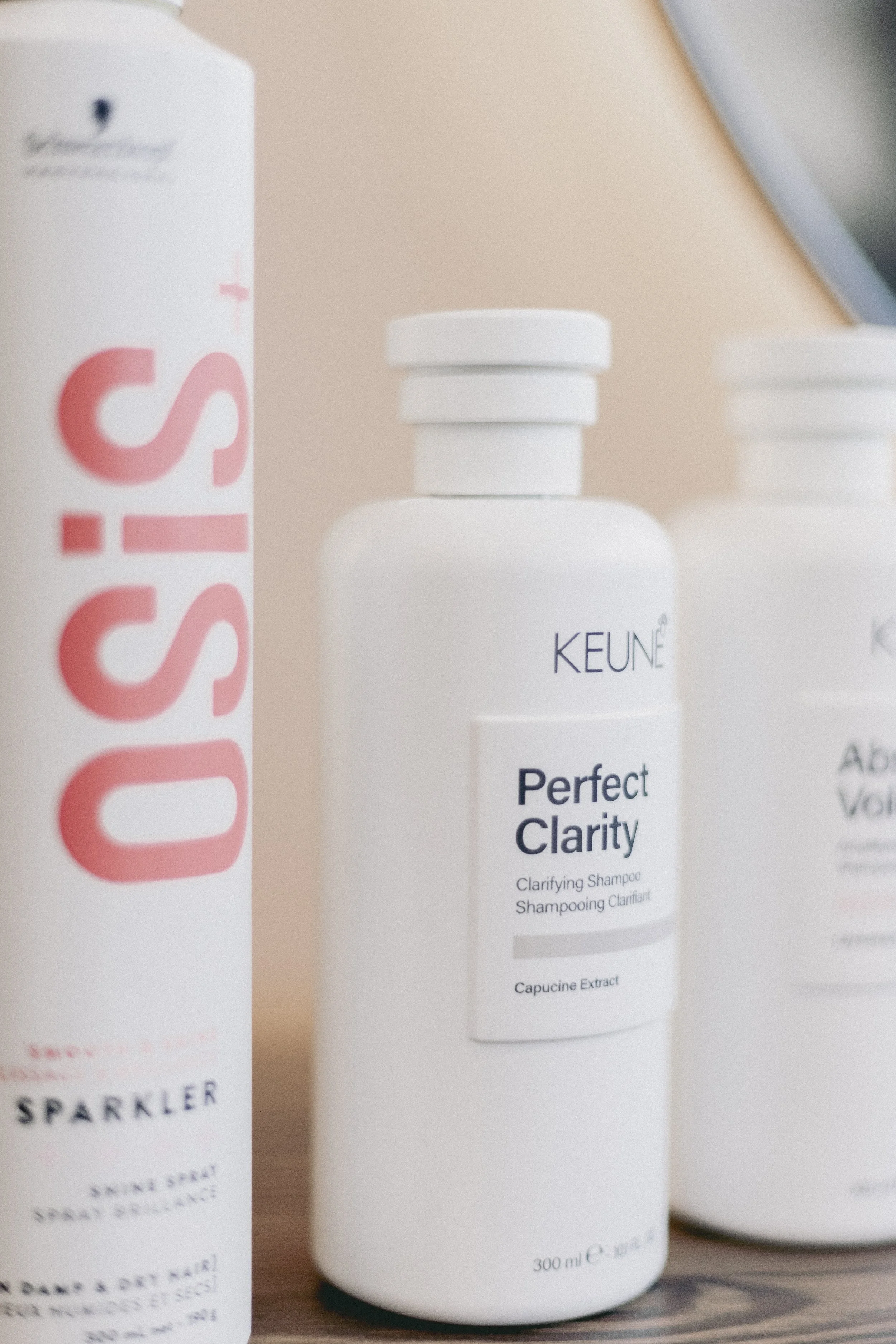 Une bouteille de shampoing clairvoyant de la marque KEUNE avec le nom 'Perfect Clarity' écrit dessus, et une boîte à côté avec une inscription partielle dans des lettres roses. La bouteille est blanche avec un capuchon blanc et 300 ml de contenu.