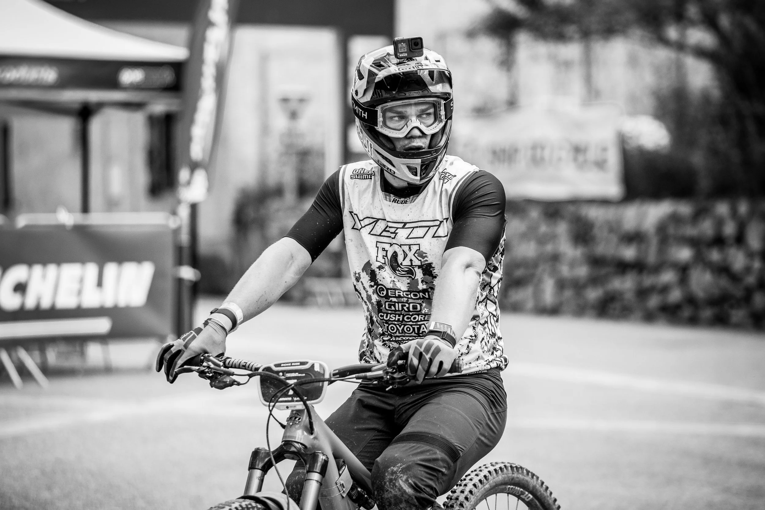 Un cycliste en tenue de protection avec un casque et des lunettes, prêt à faire du VTT en plein air, en noir et blanc.