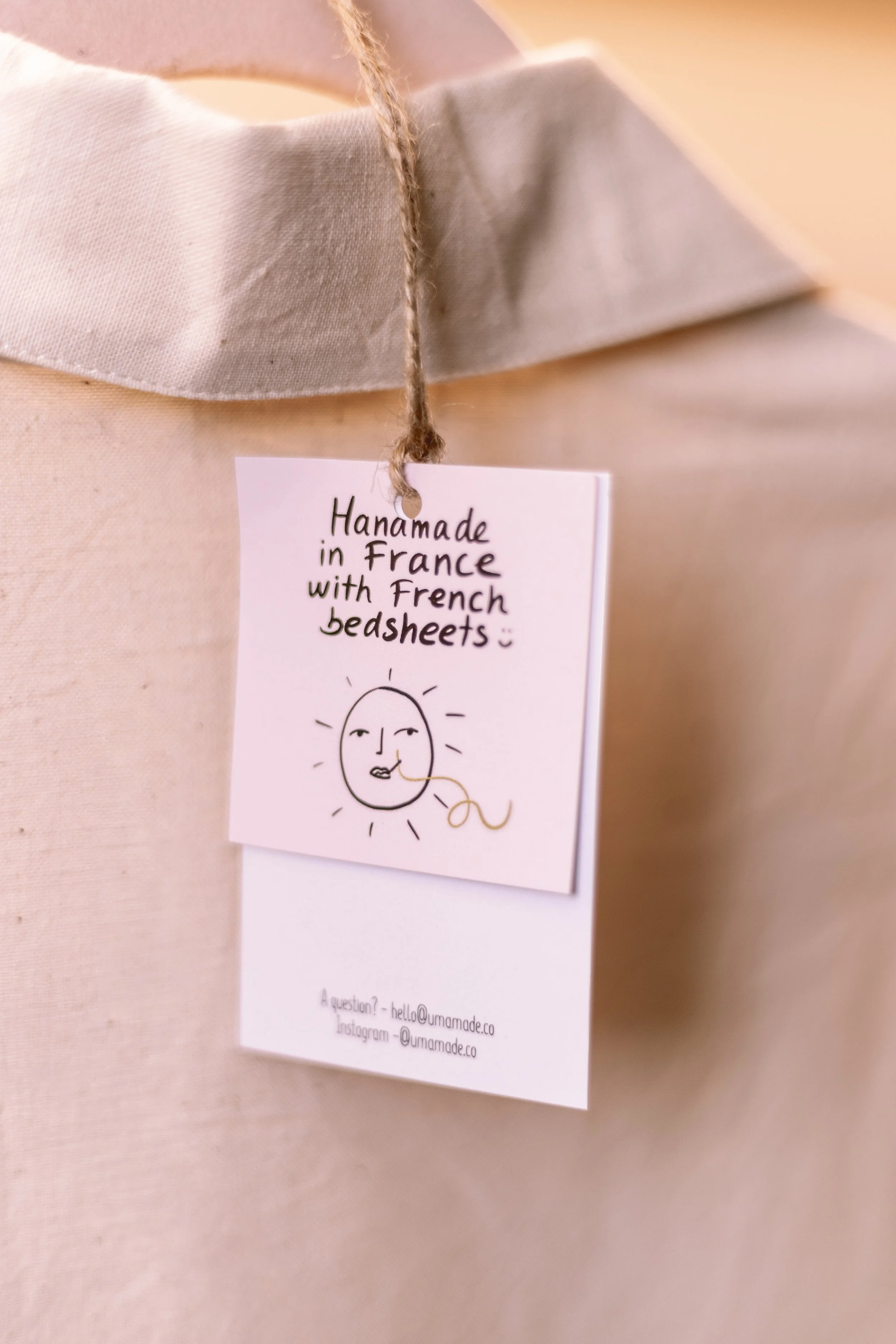 Une carte avec un dessin d'un visage souriant dans le style d'un soleil, accompagnée du texte "Hanamade in France with French bed sheets"