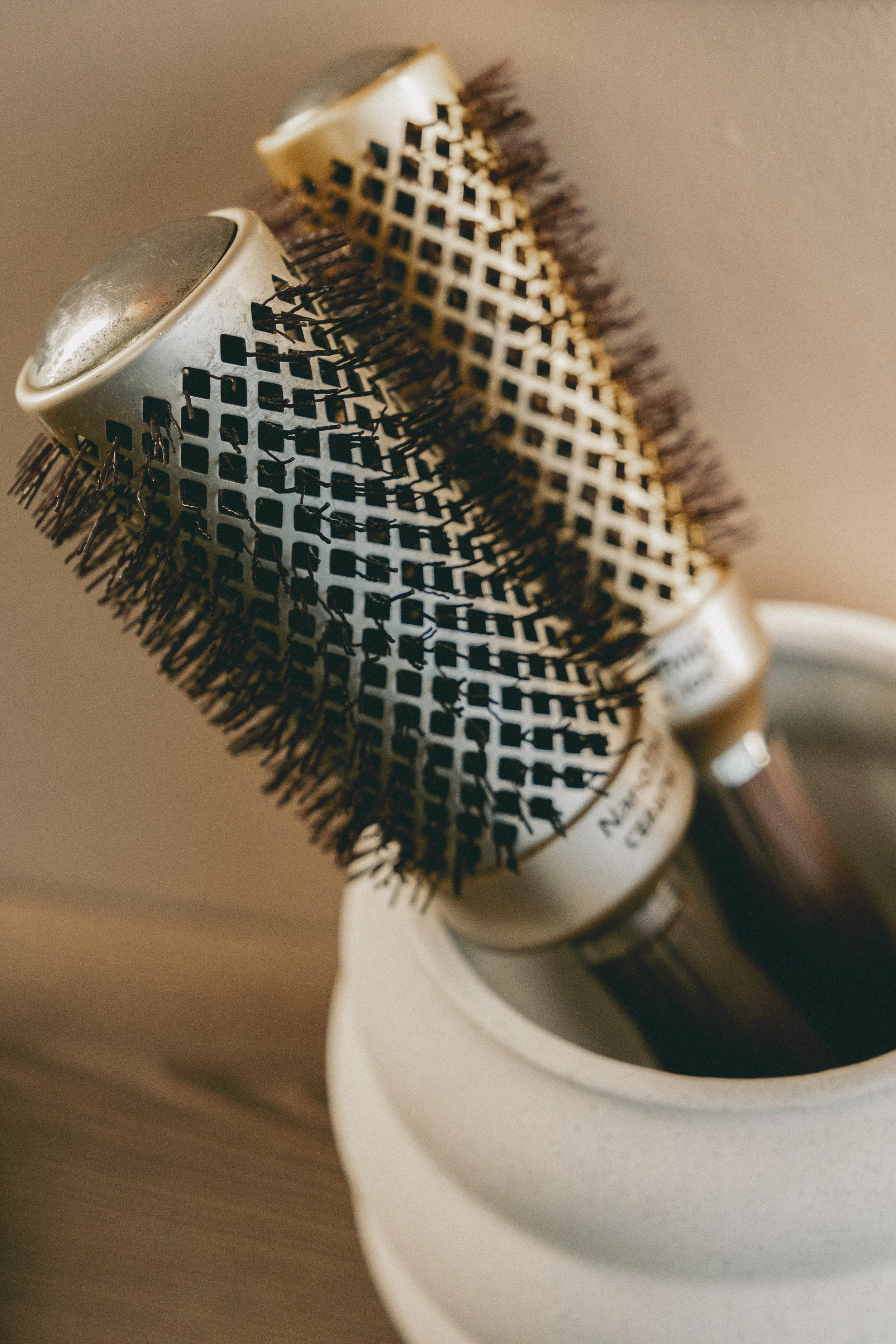 Un sèche-cheveux professionnel noir et beige avec des grilles en métal, placé dans un support en céramique blanche.
