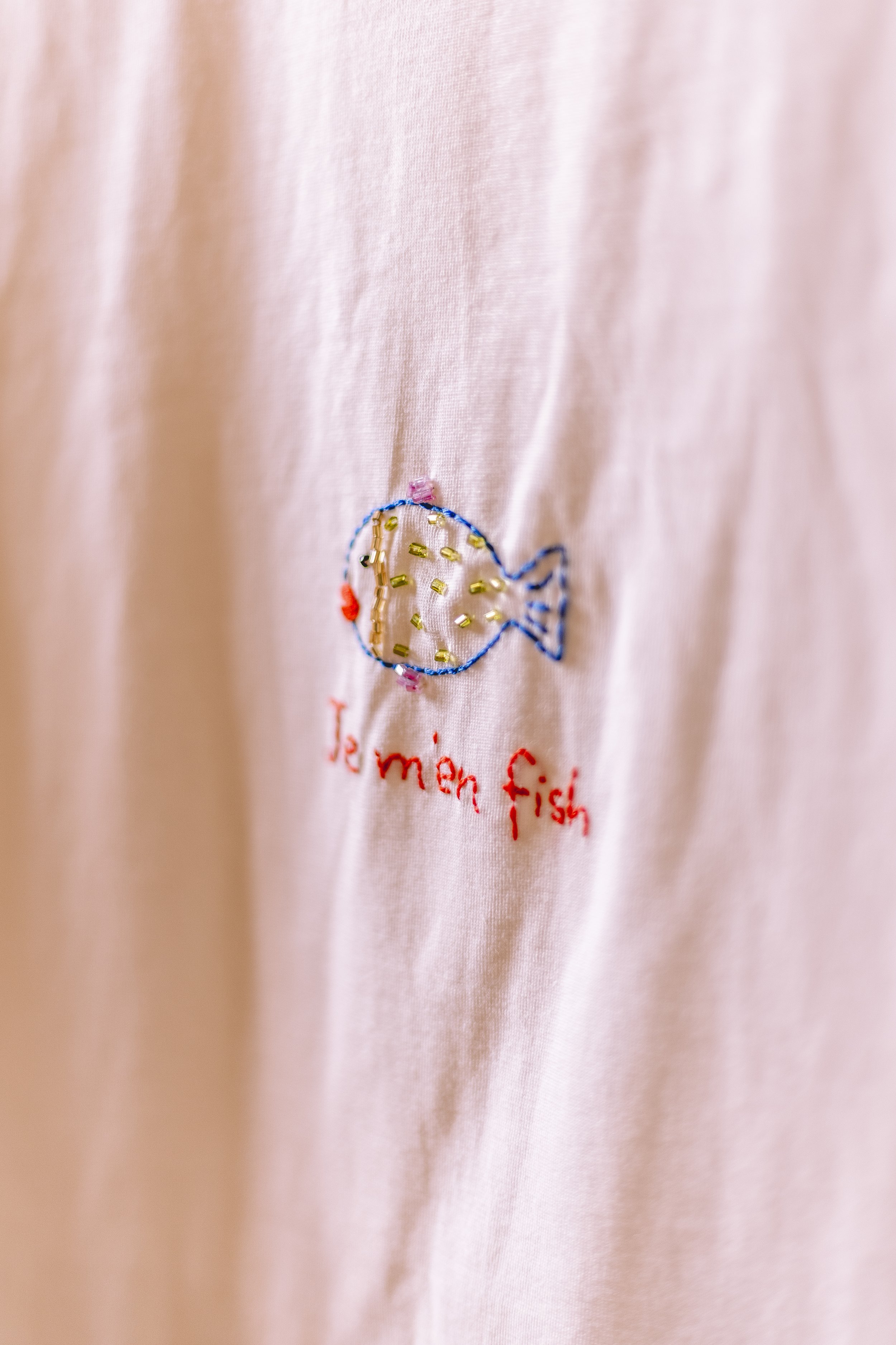 Un tissu rose avec une broderie d'un poisson en fil coloré et le texte "dernier poisson" en rouge.