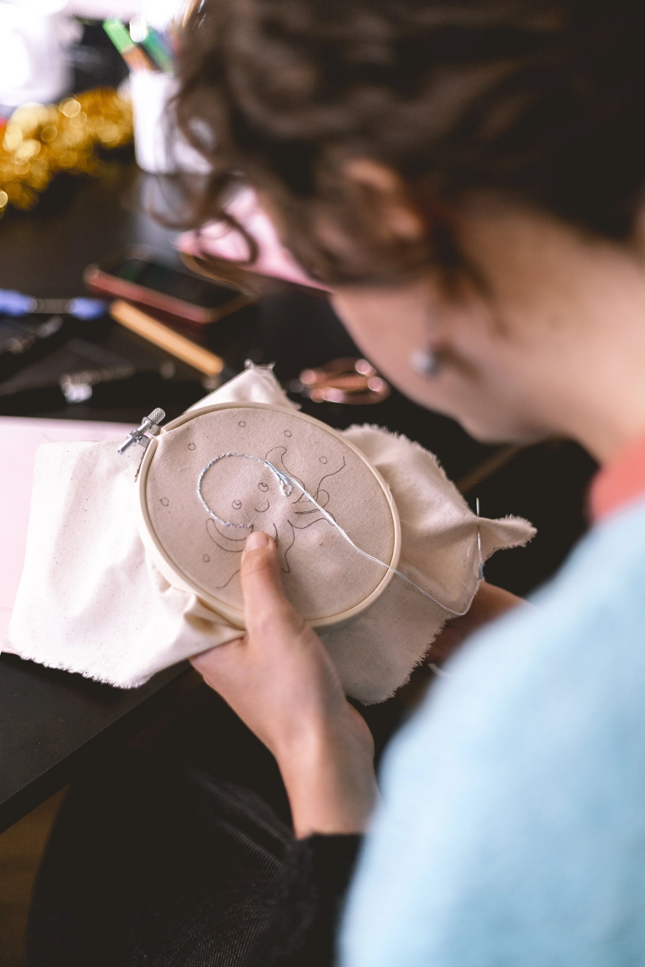 Une personne brode un dessin d'un poulpe sur une toile. La scène se déroule probablement dans un atelier ou lors d'une activité de couture.