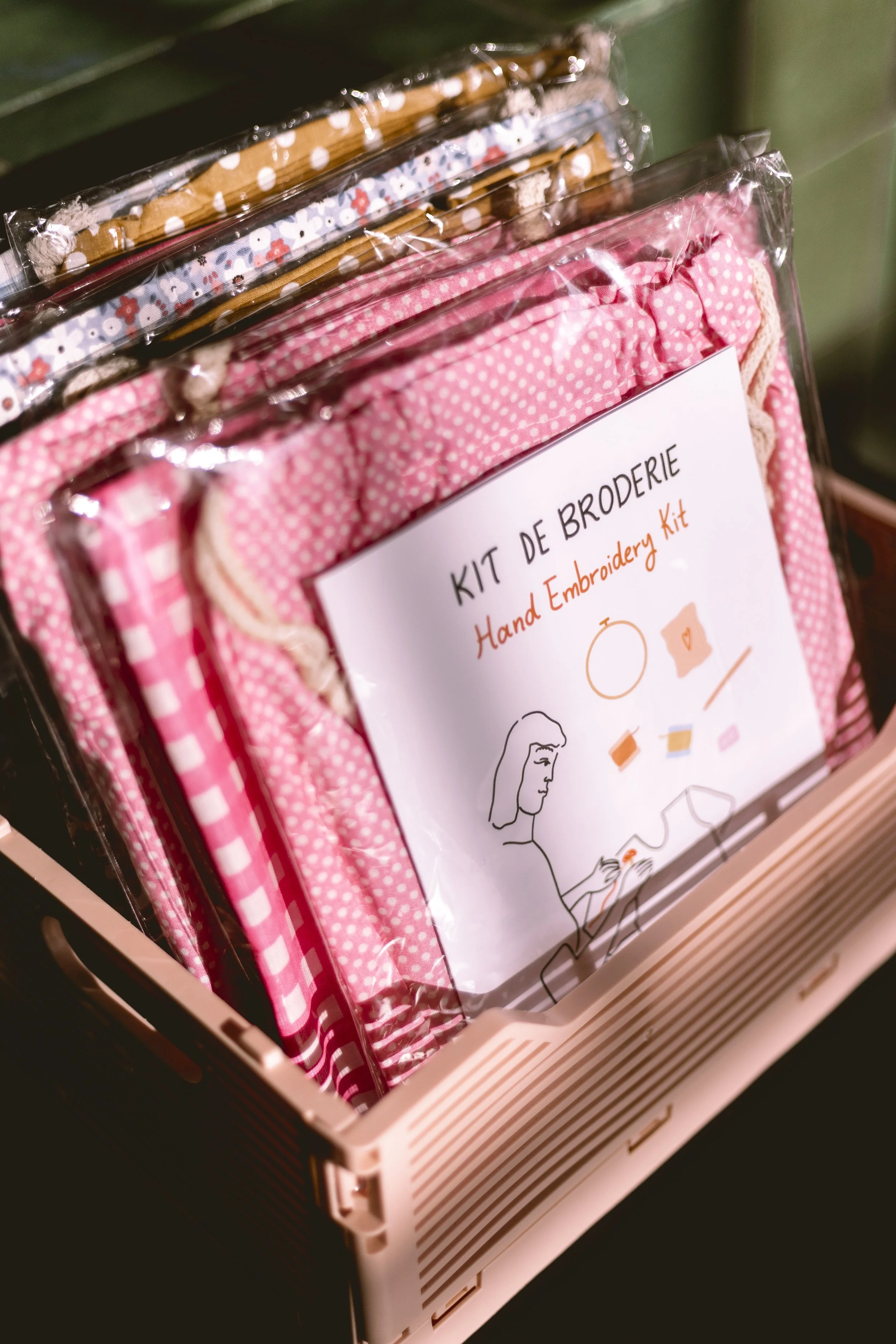 Un kit de broderie pour le point de croix dans une boîte en plastique avec des tissus roses et des instructions illustrées.