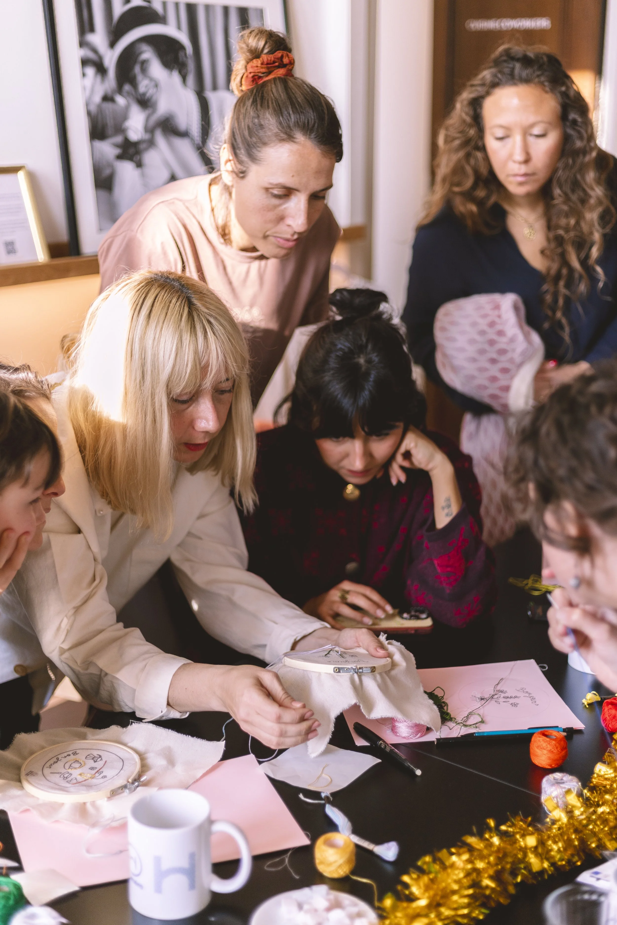 Groupe de femmes autour d'une table en train de coudre et de travailler sur des projets de broderie, avec des fournitures de couture et décoration de fête