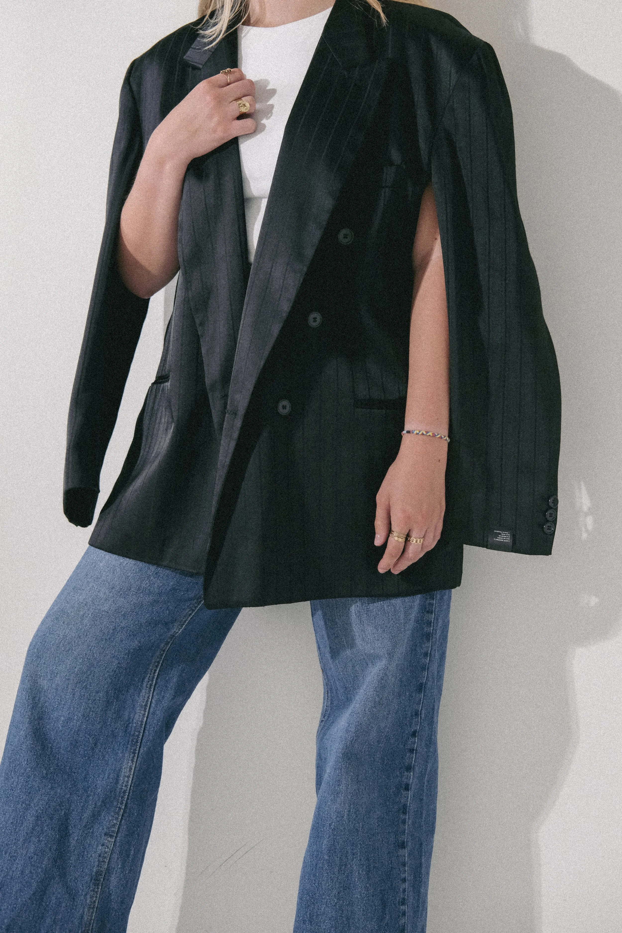 Femme portant un blazer noir en lin avec une chemise blanche et un jean bleu, tenant sa veste d'une main.