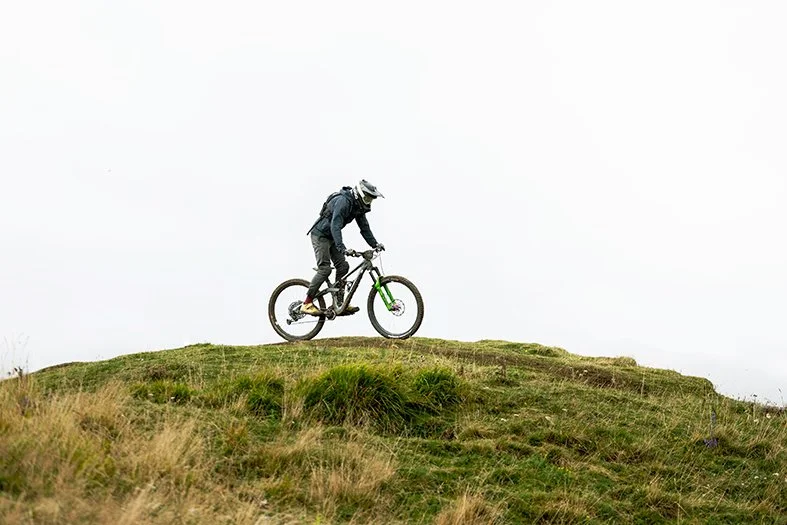 Cliché d'une personne faisant du vélo tout terrain sur un terrain herbeux avec un ciel clair en arrière-plan.