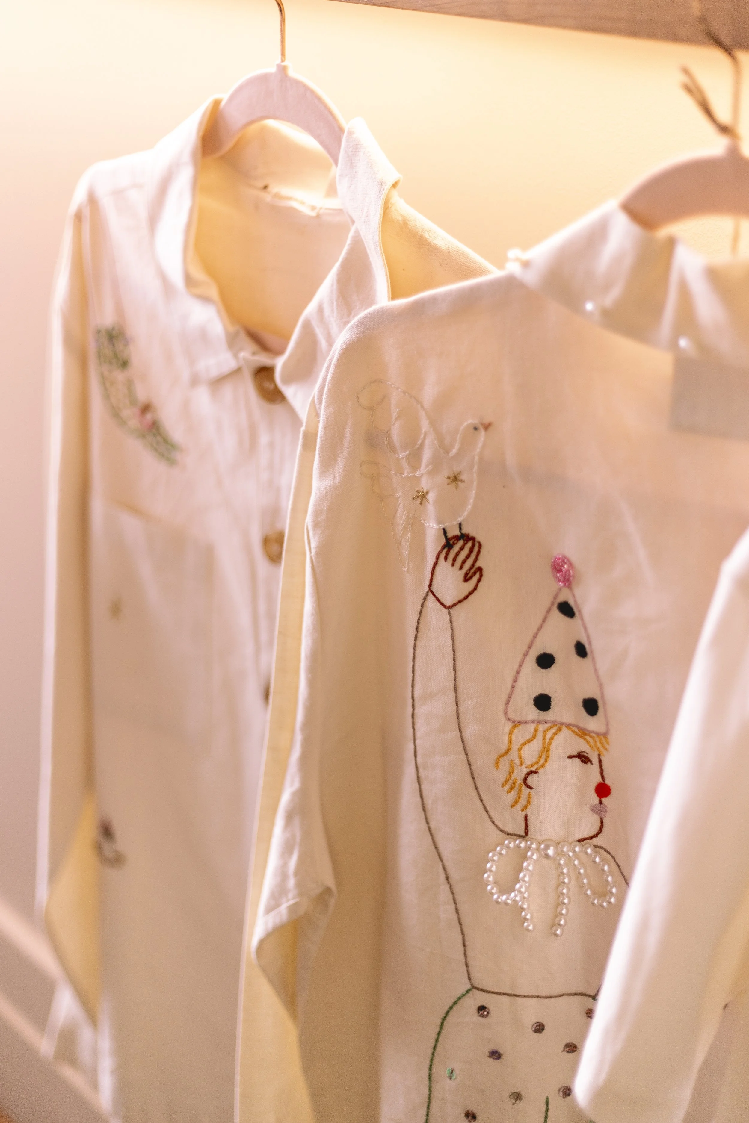 Vêtements pour enfants suspendus avec des broderies et des décorations de princesse, comprenant une robe avec un motif de princesse et une princesse en filigrane avec un chapeau pointu, décorée de perles et de paillettes.